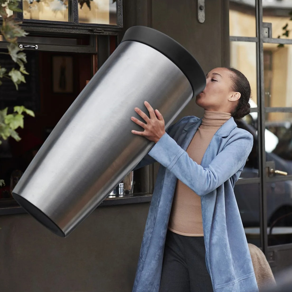 woman drinking coffee from large travel mug at take away counter of cafe