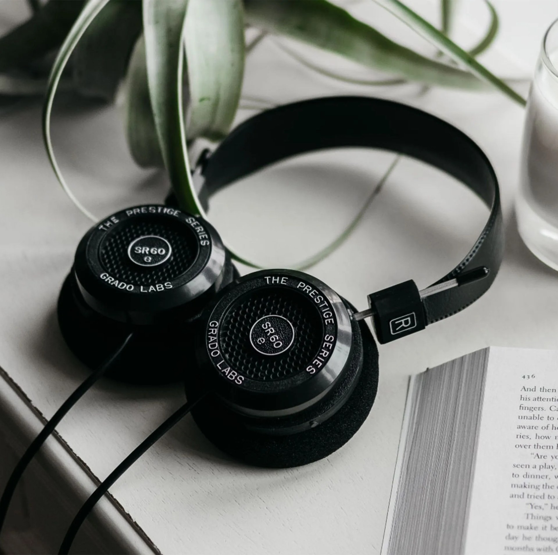 grado black headphones laying against white counter with a candle and book