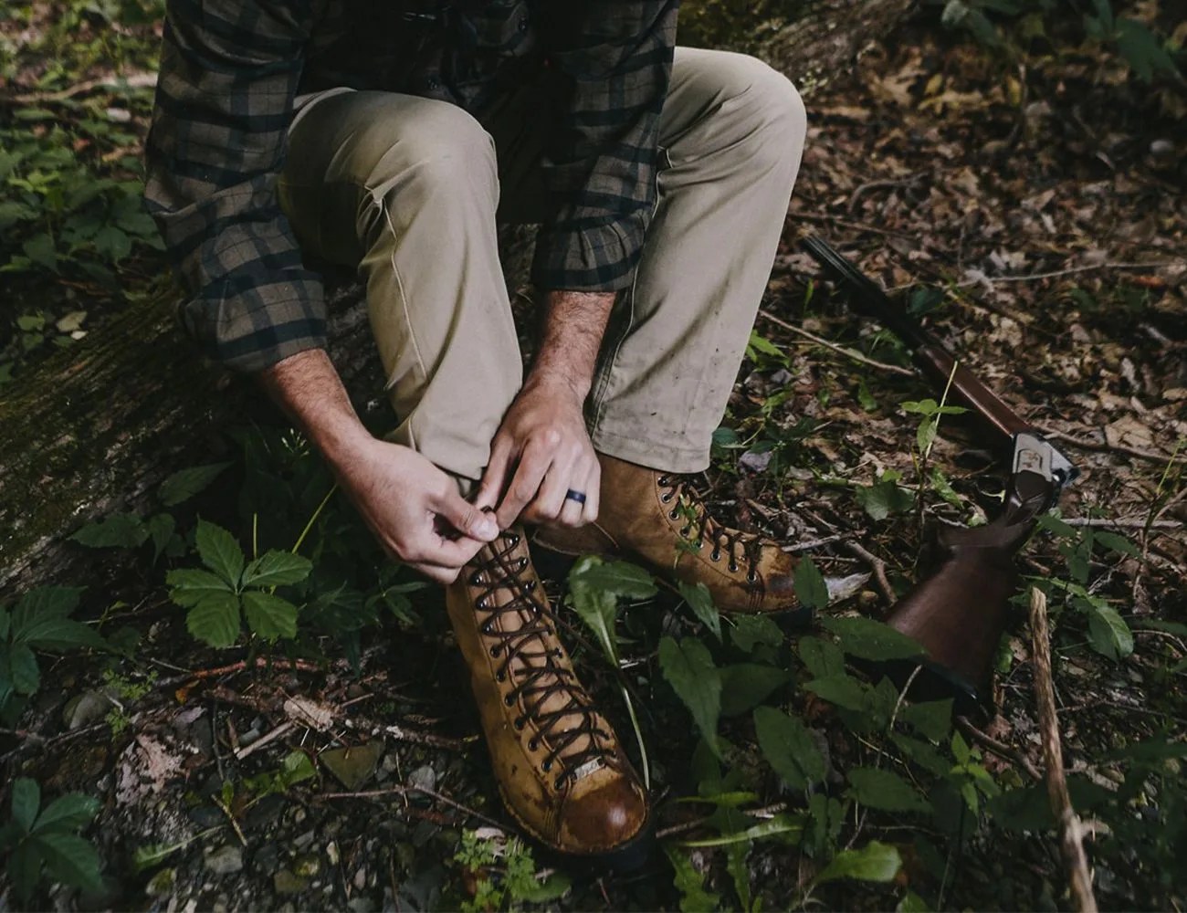 man lacing up danner boots in the woods