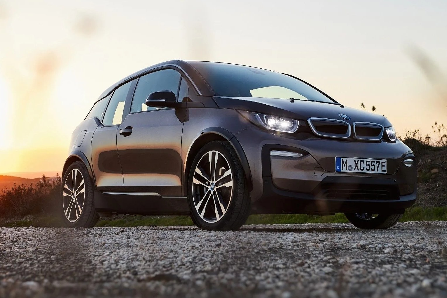 bmw i3 parked on pavement in front a meadow with a sunset in the background