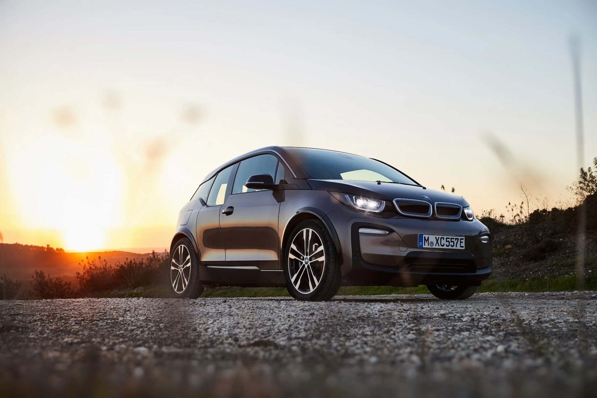 bmw i3 parked on pavement in front a meadow with a sunset in the background