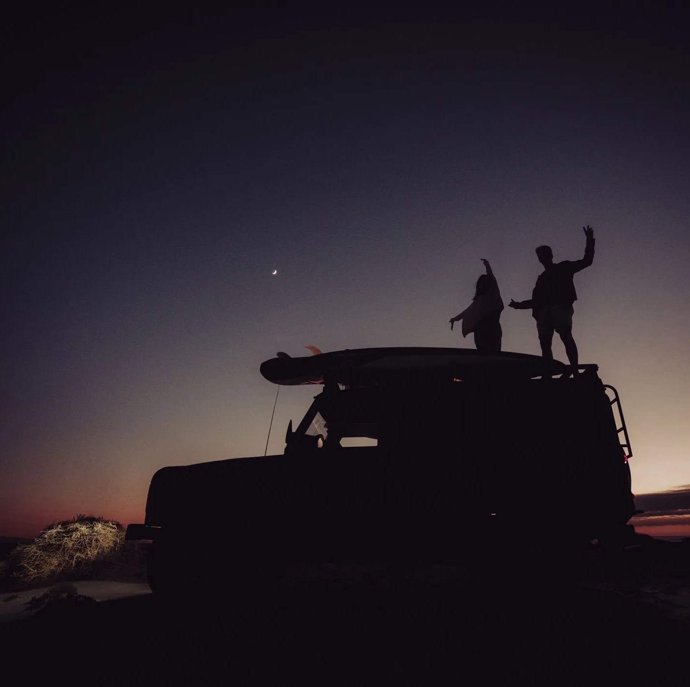 couple standing on top of a 4x4 while camping during the blue hour