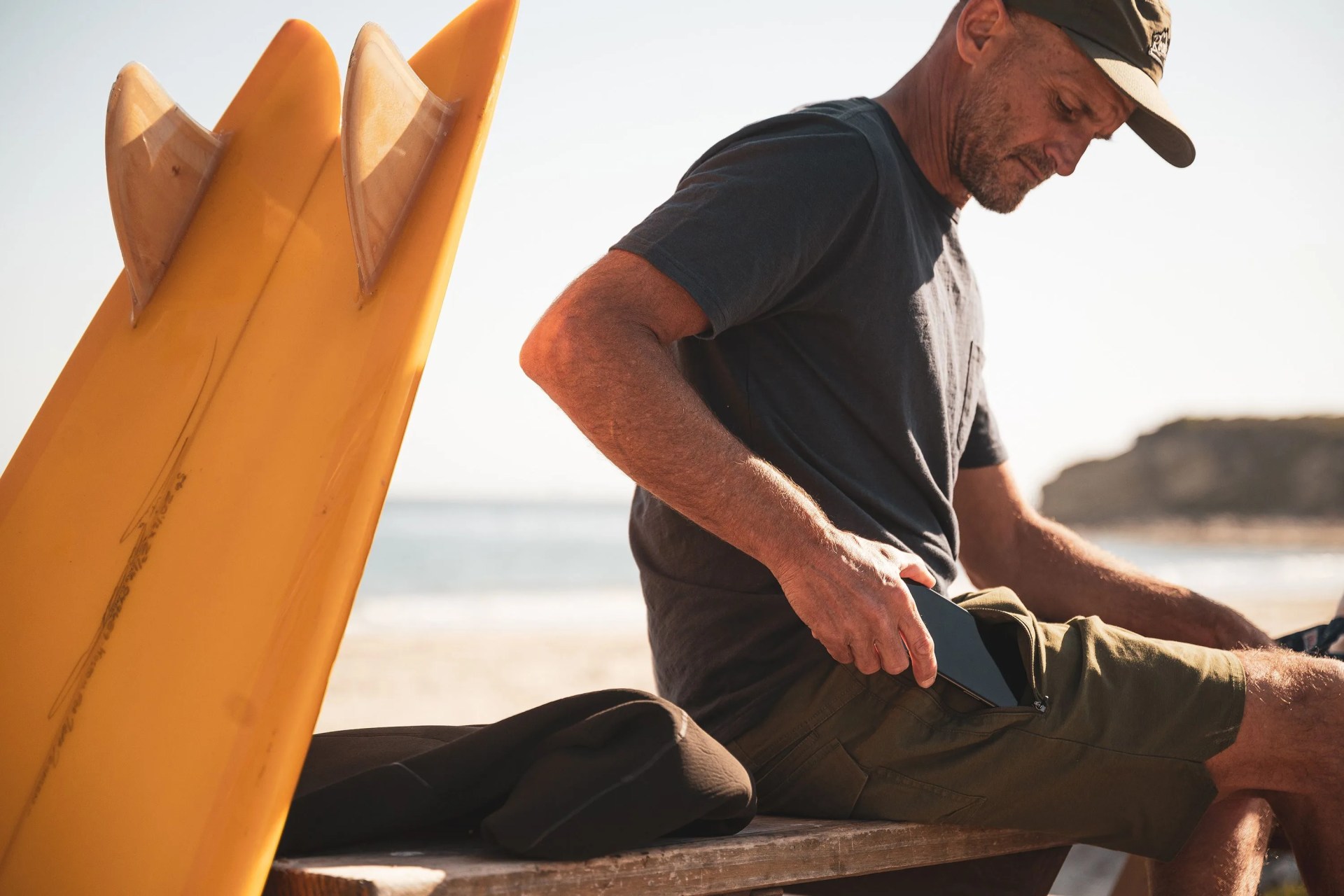 man wearing tan roark shorts sitting down pulling out his phone