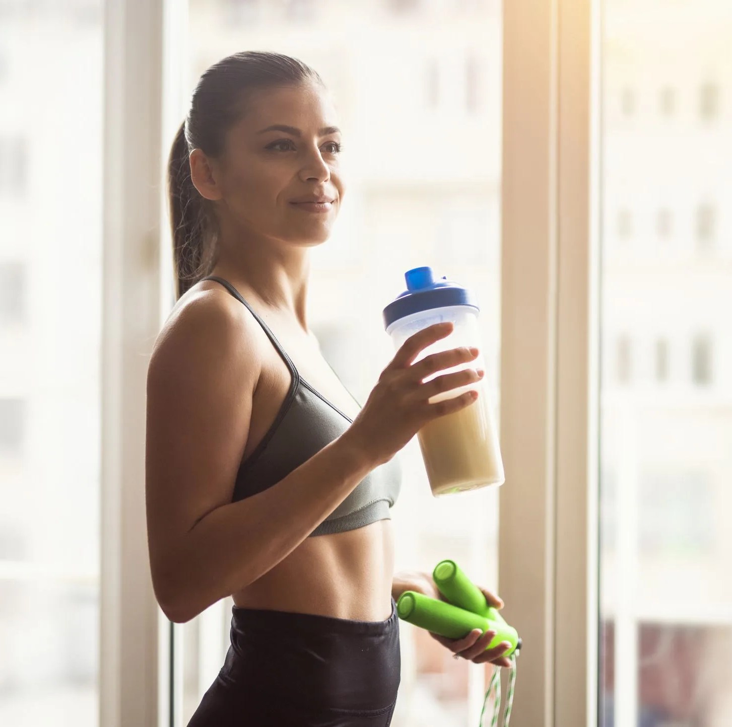 young female athlete drinking protein shake after workout