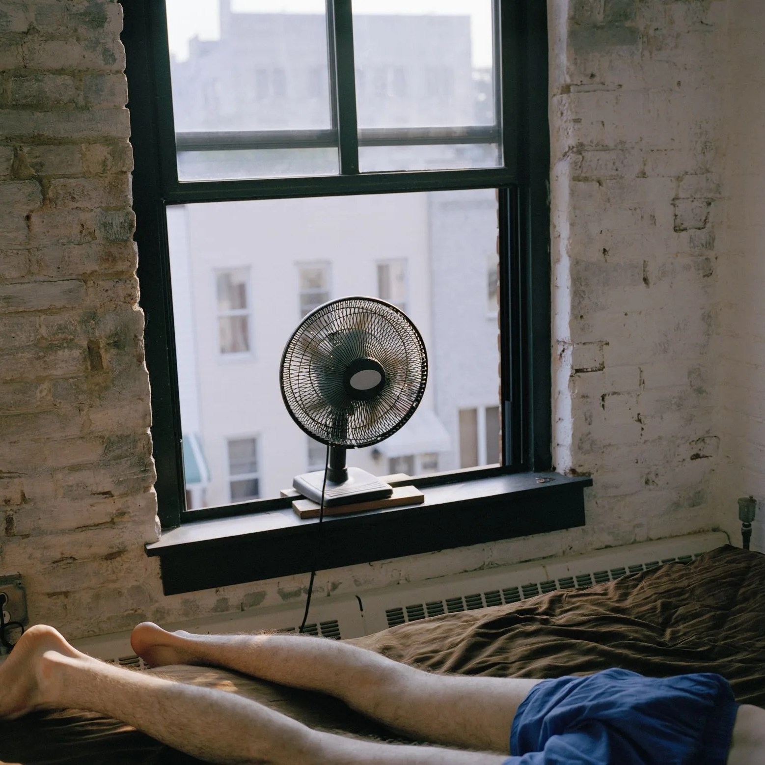 a man lying on a bed with a fan blowing