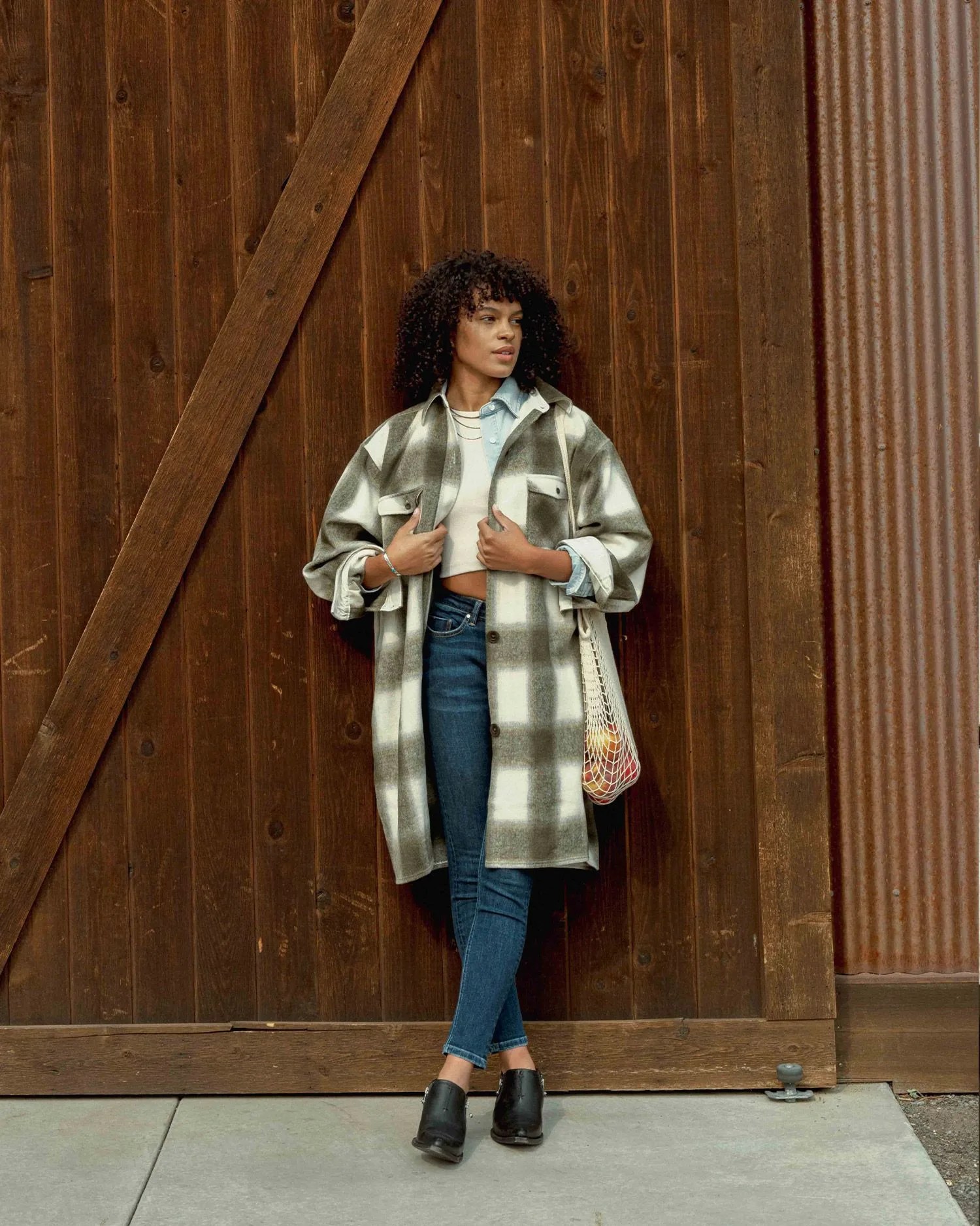 woman adjusting coat while leaning against wall
