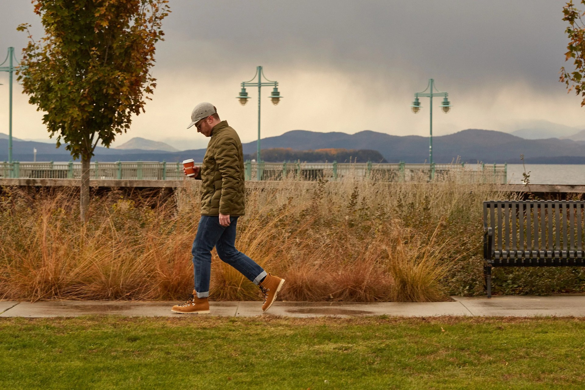 man walking holding coffee cup wearing aether jacket