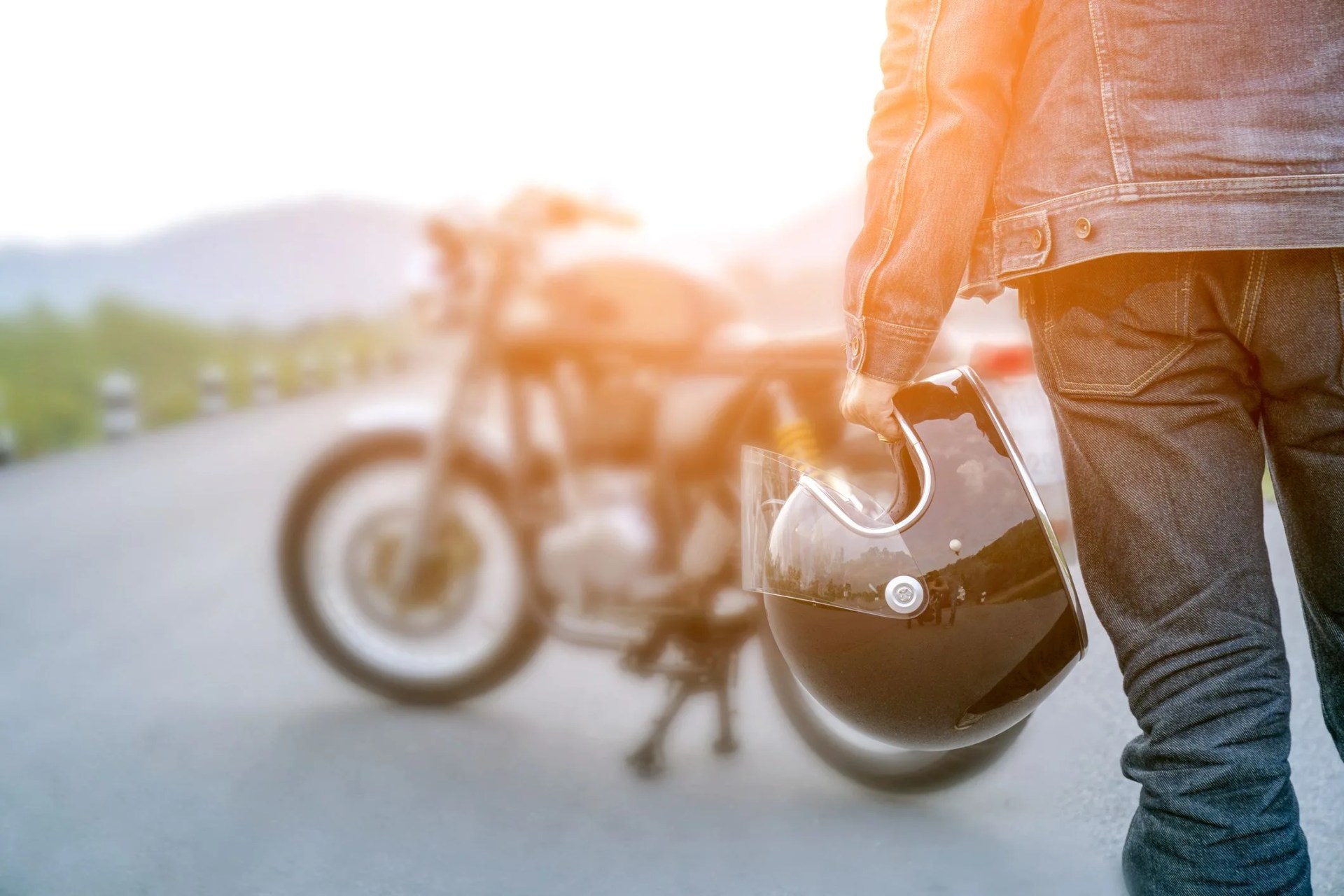 handsome man in jean is holding a helmet and vintage motorcycle blur background