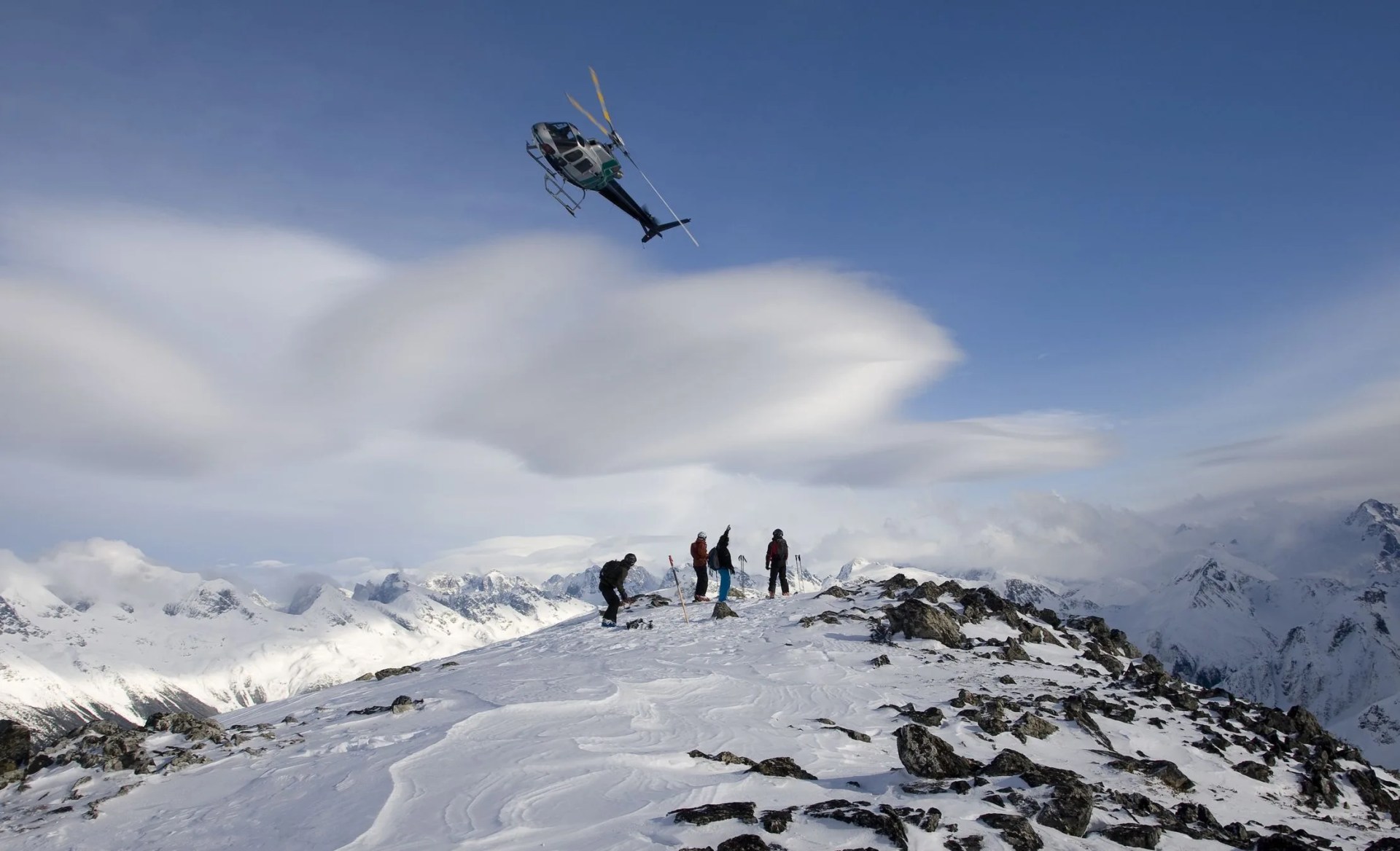 helicopter flies of skiers on mountain top