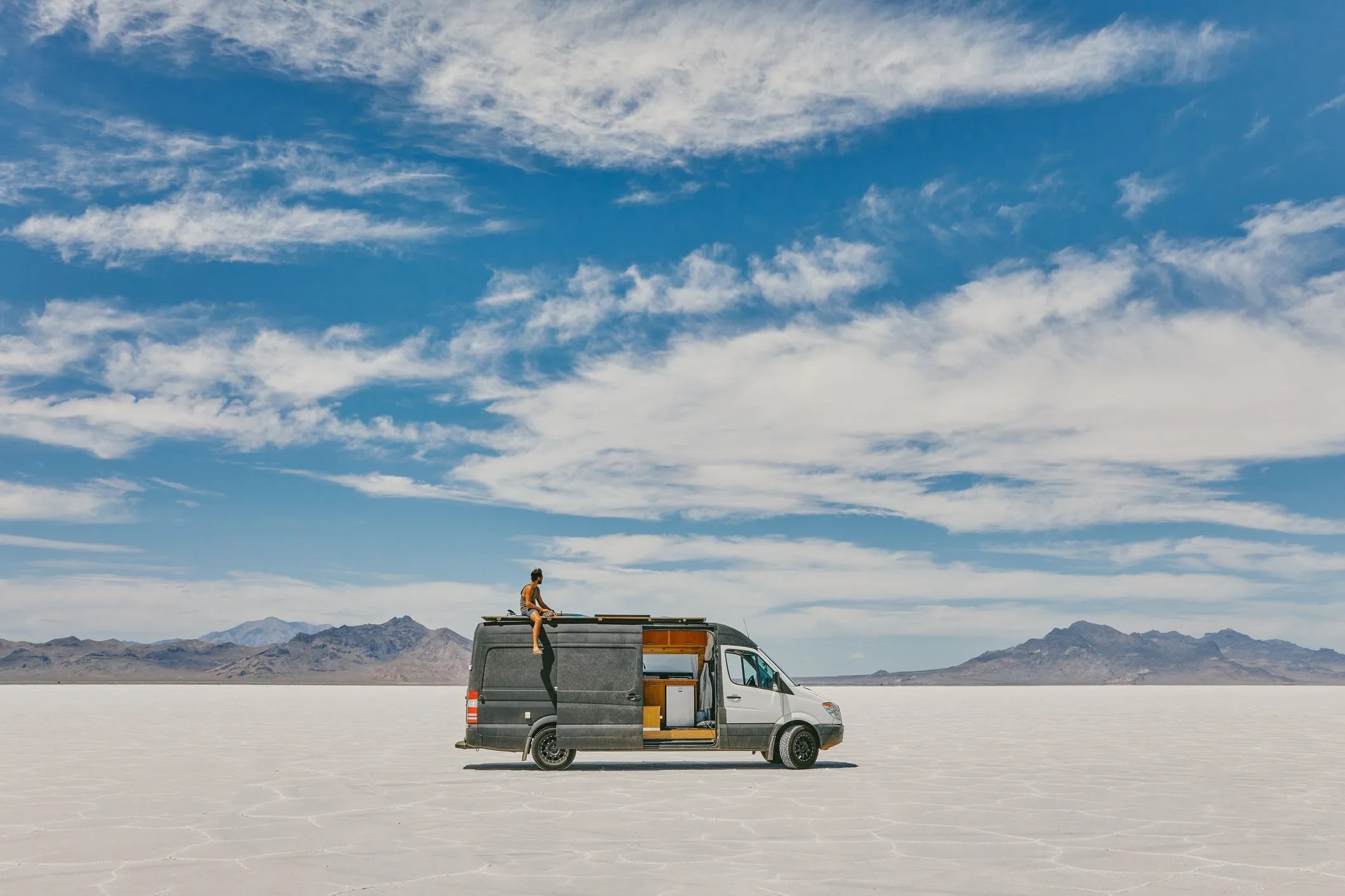 young man sitting on roof of camper van in bonneville salt flats
