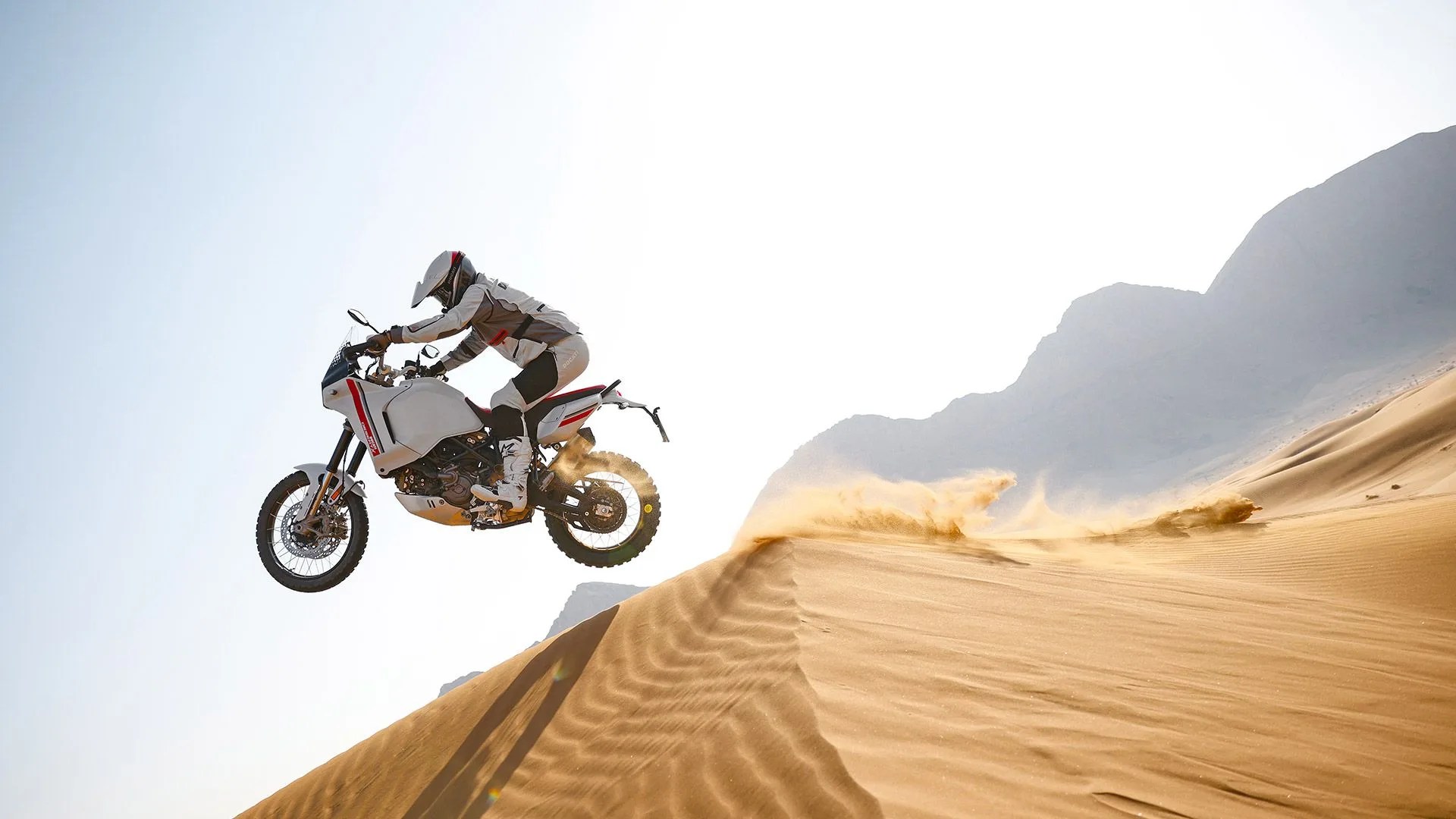 person riding ducati desertx white motorcycle on sand dunes