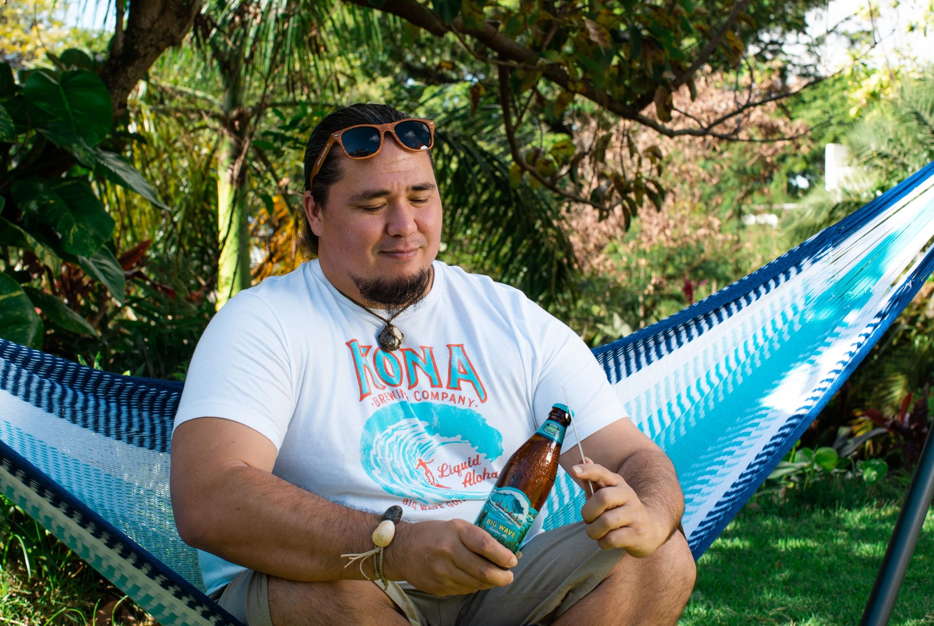 man sitting in kona gameday hammock opening a beer