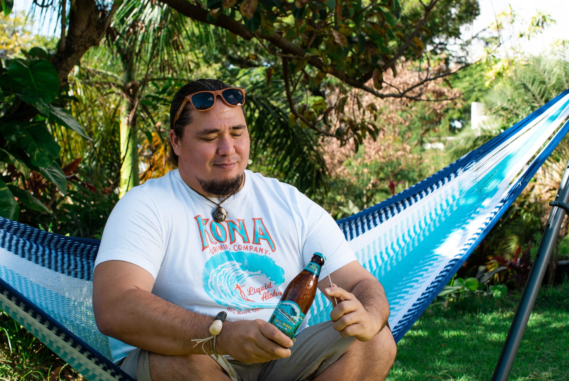 man sitting in kona gameday hammock opening a beer