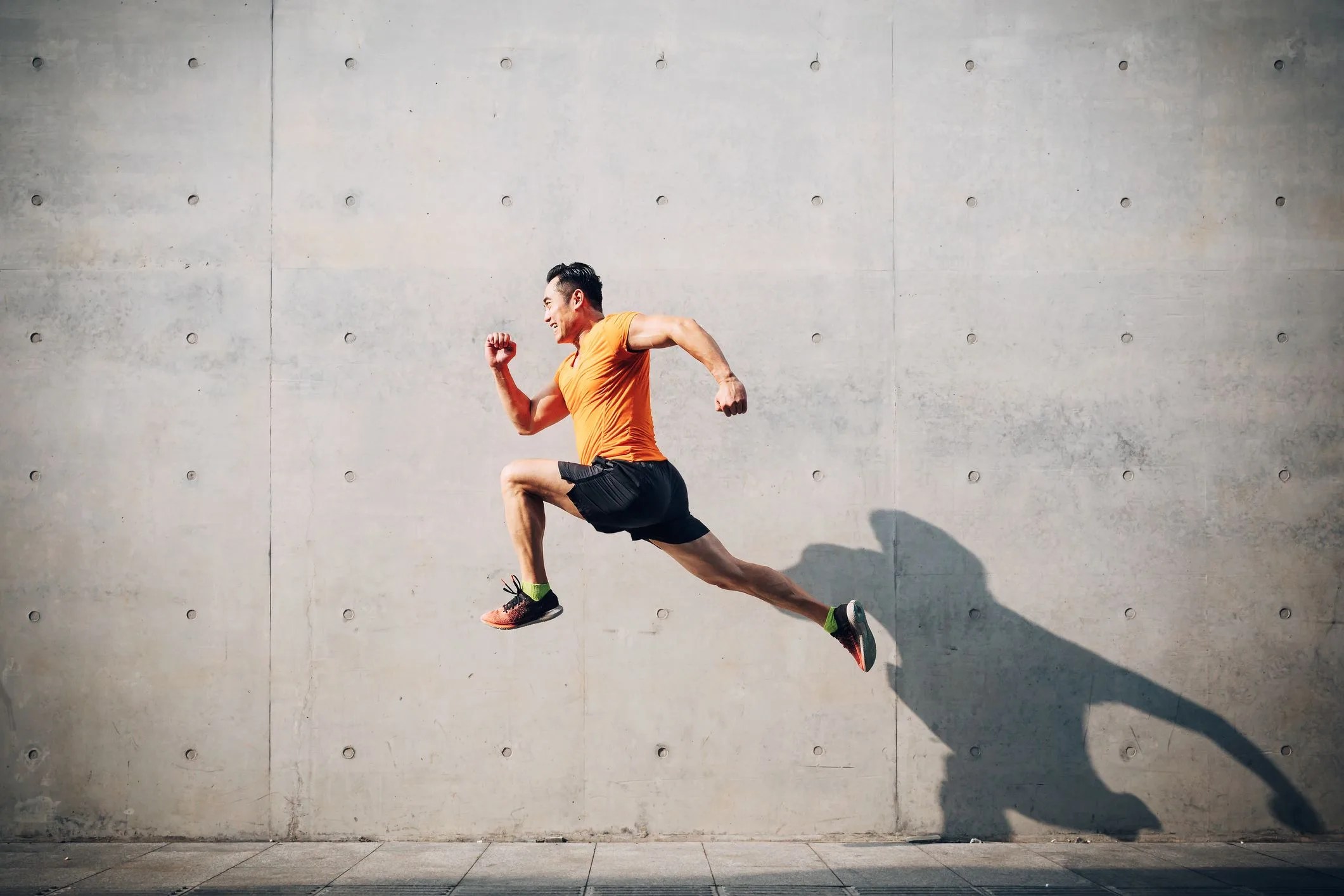 sporty asian mid man running and jumping against shutter