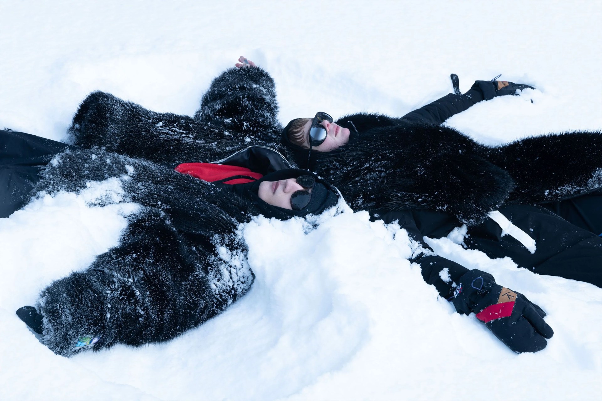 two people wearing vuarnet sunglasses laying down in the snow next to each other