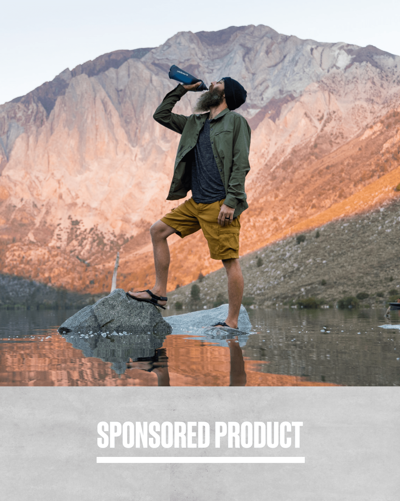 sponsored product man standing with one leg on a rock while drinking from lifestraw water container with mountains in the background