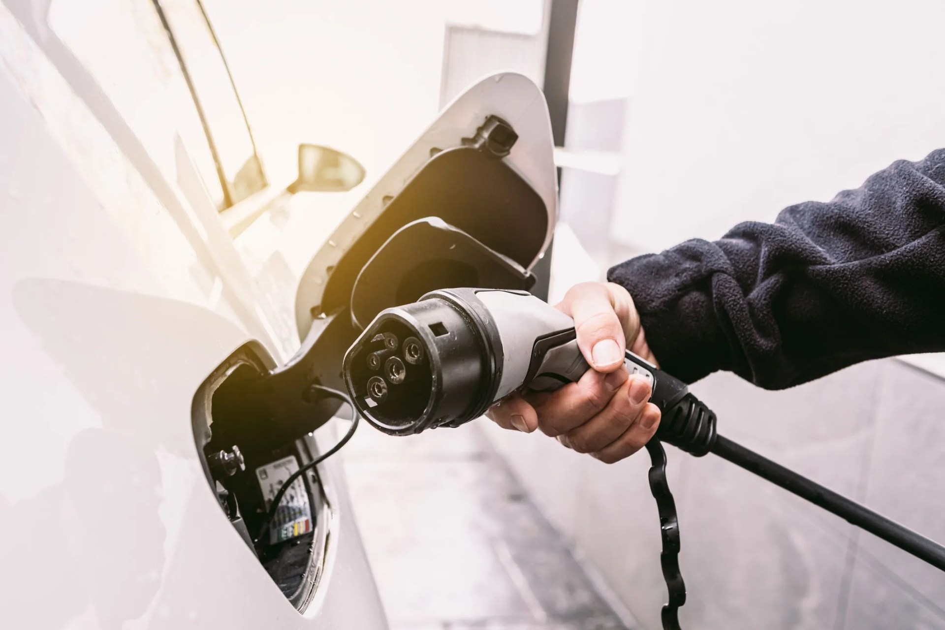 detail of a hand plugging the cord into an electric car, to charge the battery in the garage outside a home concept of electric car charging, renewable energy, sustainability and transport