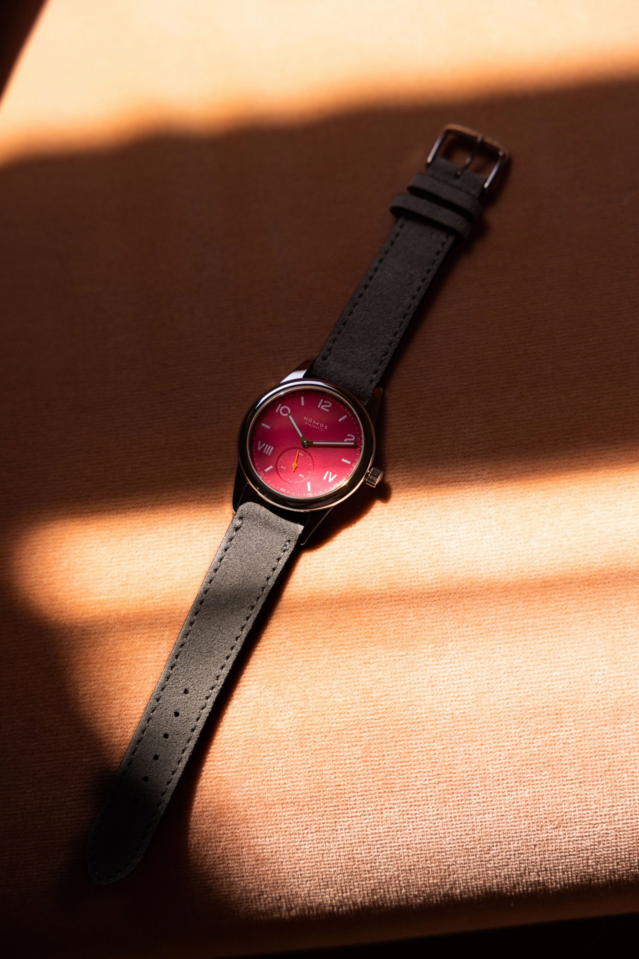 nomos watch laying on fabric with pink dial
