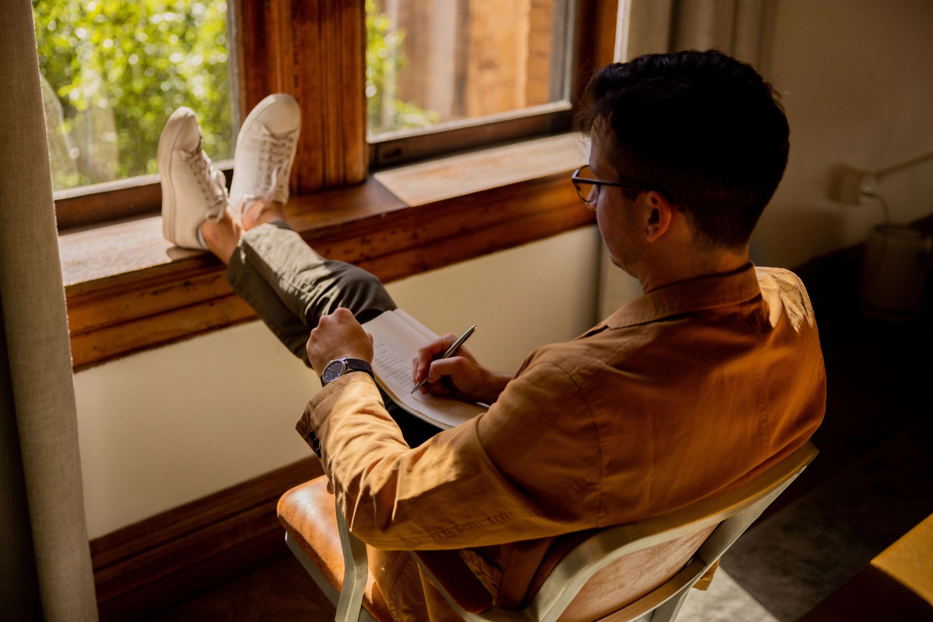 man sitting in chair writing with feet propped up wearing nomos watch
