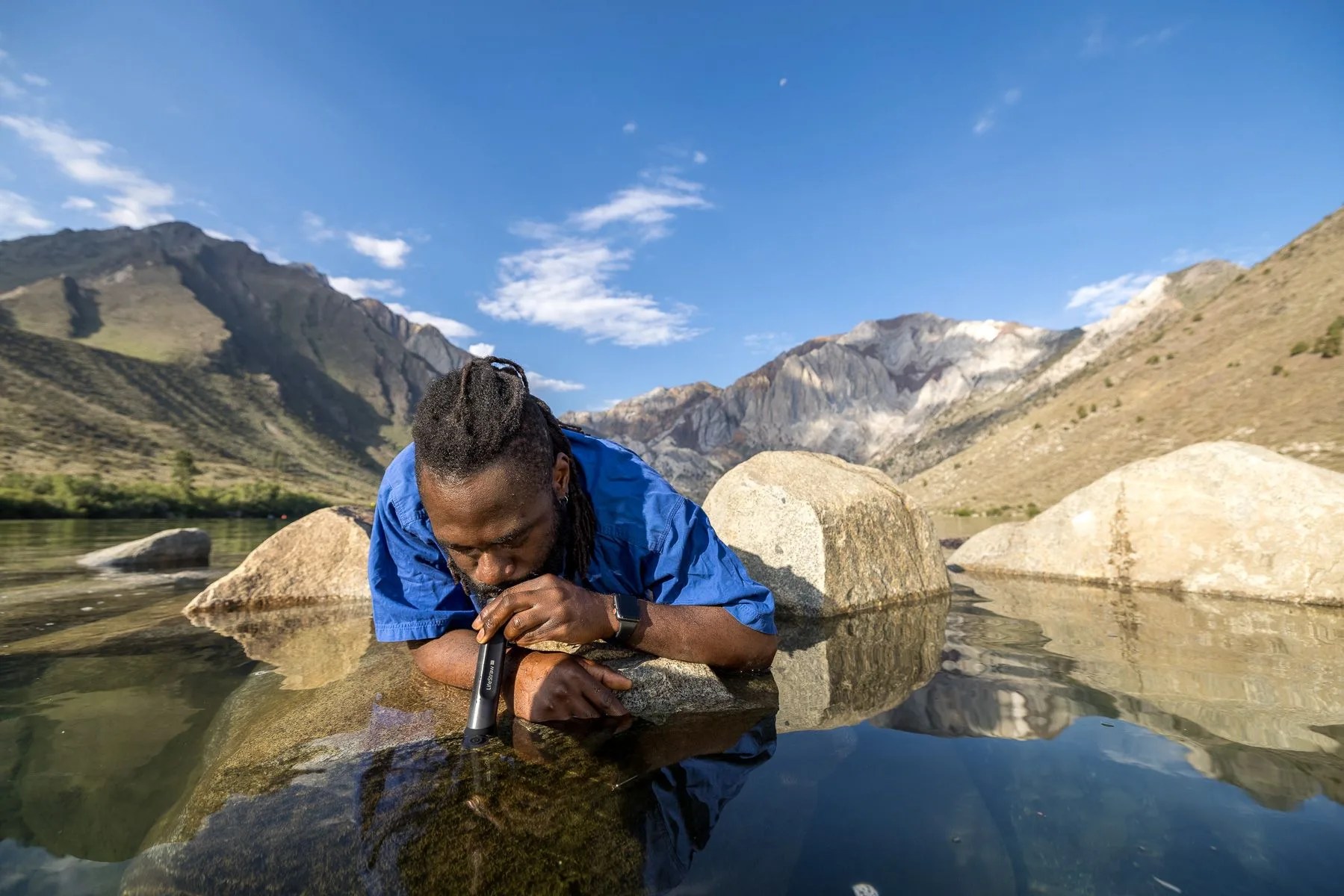 man drinking out of lifestraw from lake