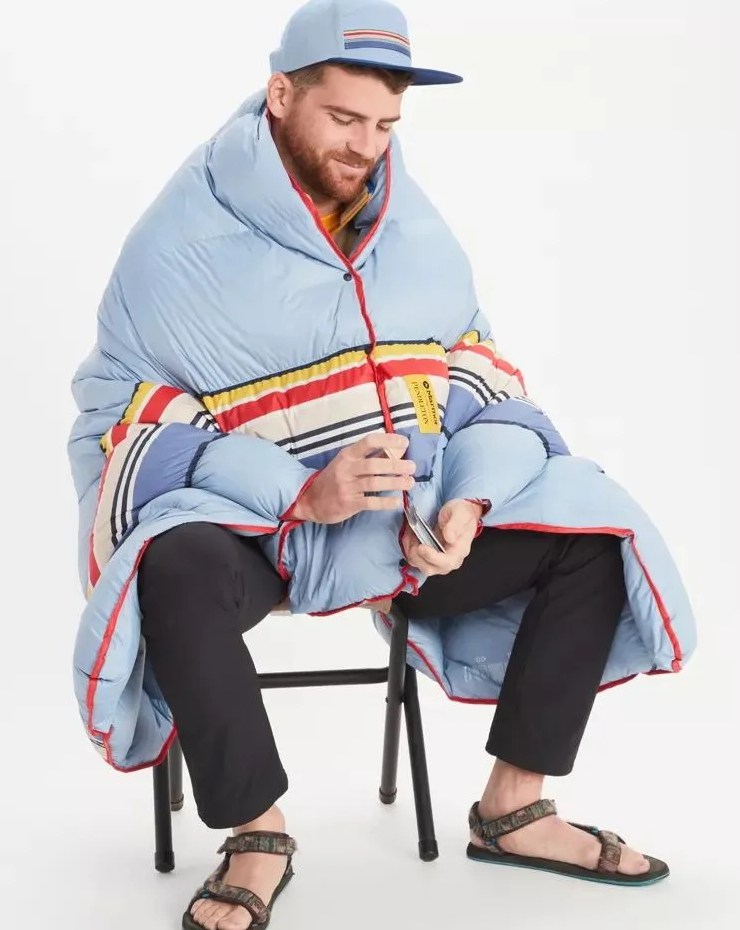 man sitting down holding some cards with marmot x pendleton down quilt wrapped around him