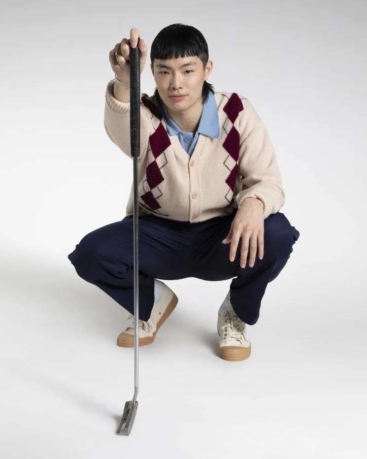 man squatting while holding golf club wearing manor argyle striped cardigan