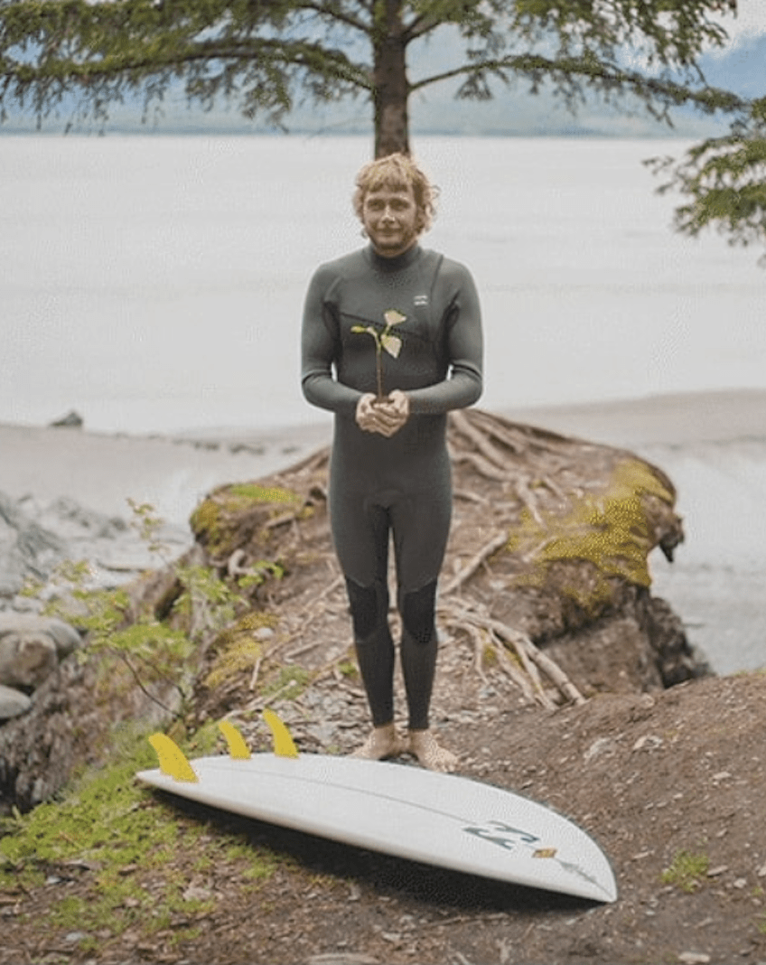 man holding a plant wearing billabong furnace natural wetsuit behind snowboard by lake