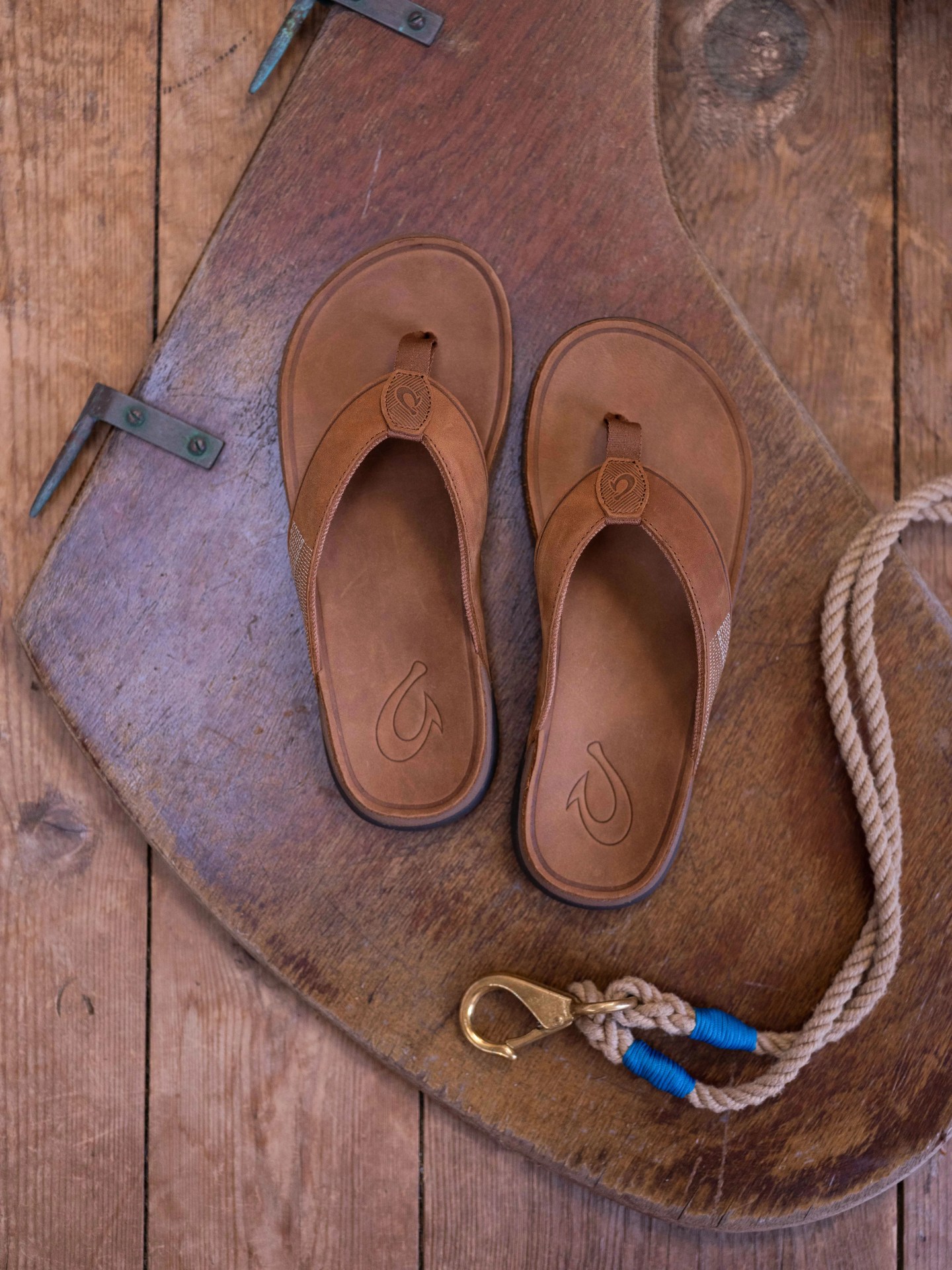 olukai tuahine sandals resting on a wooden board next to a hook attached to a rope cord