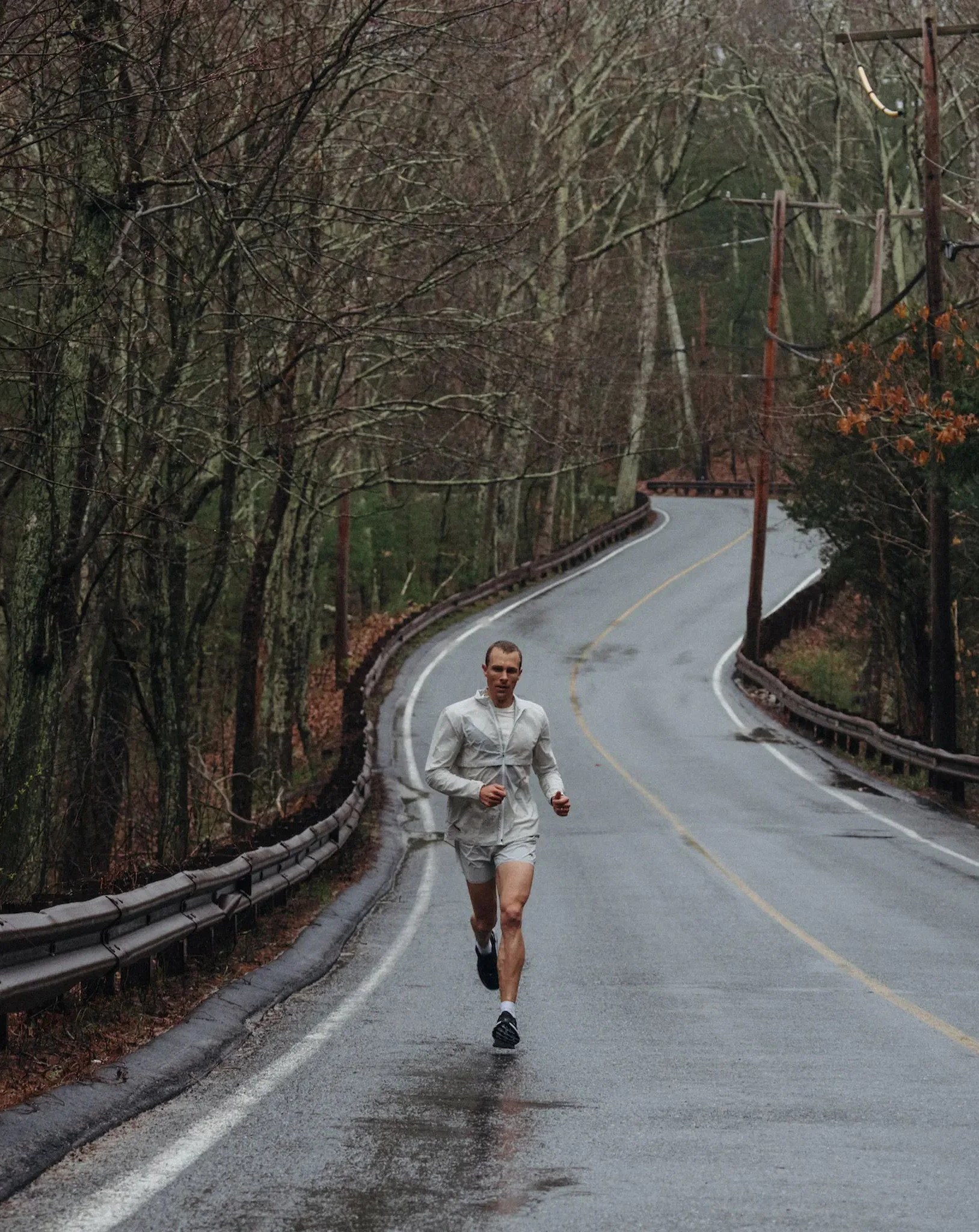 man running in rain on road by trees wearing tracksmith outfit