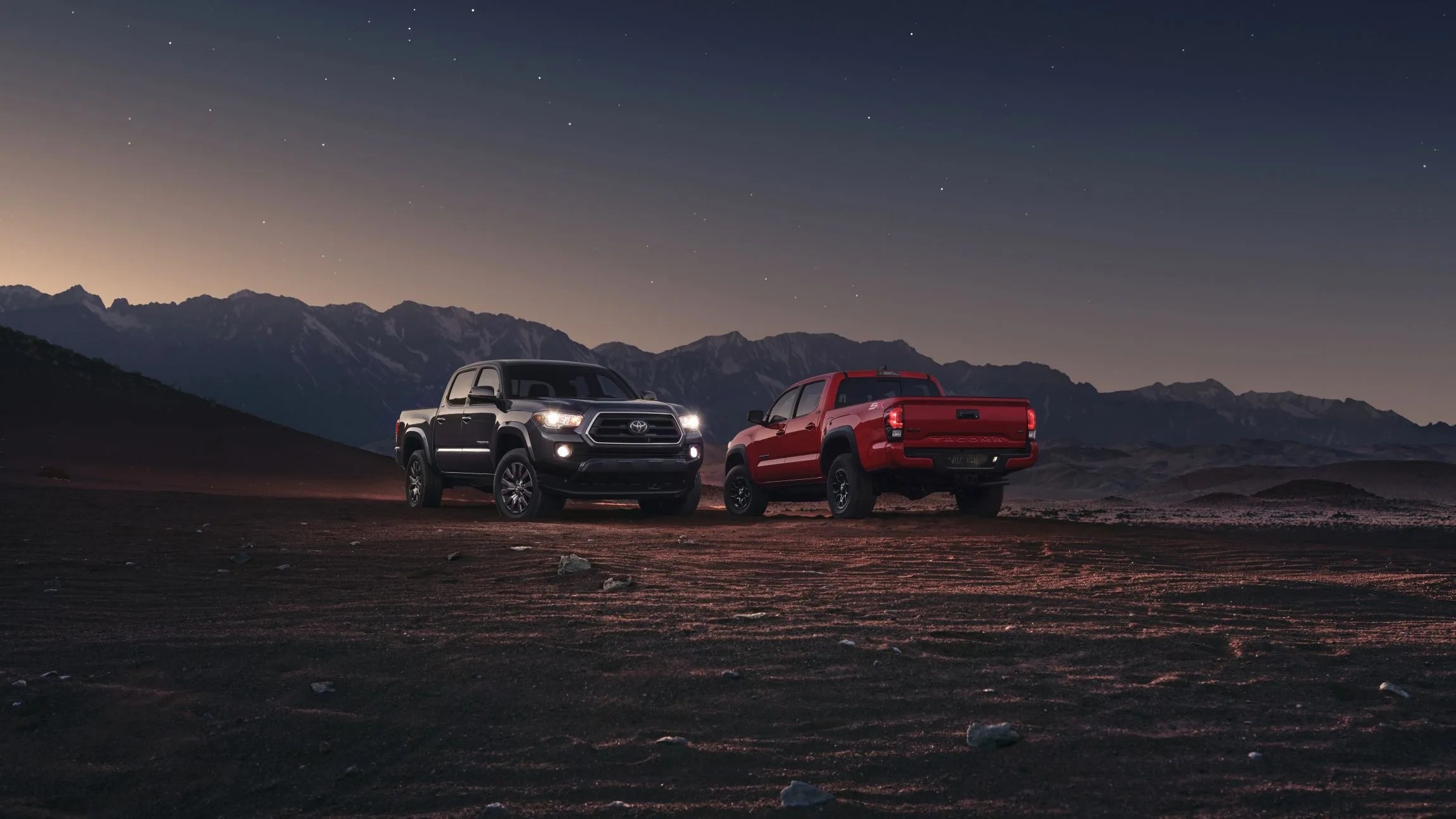 two toyota tacomas parked to display the new sx and chrome packages in the desert with a mountain backdrop