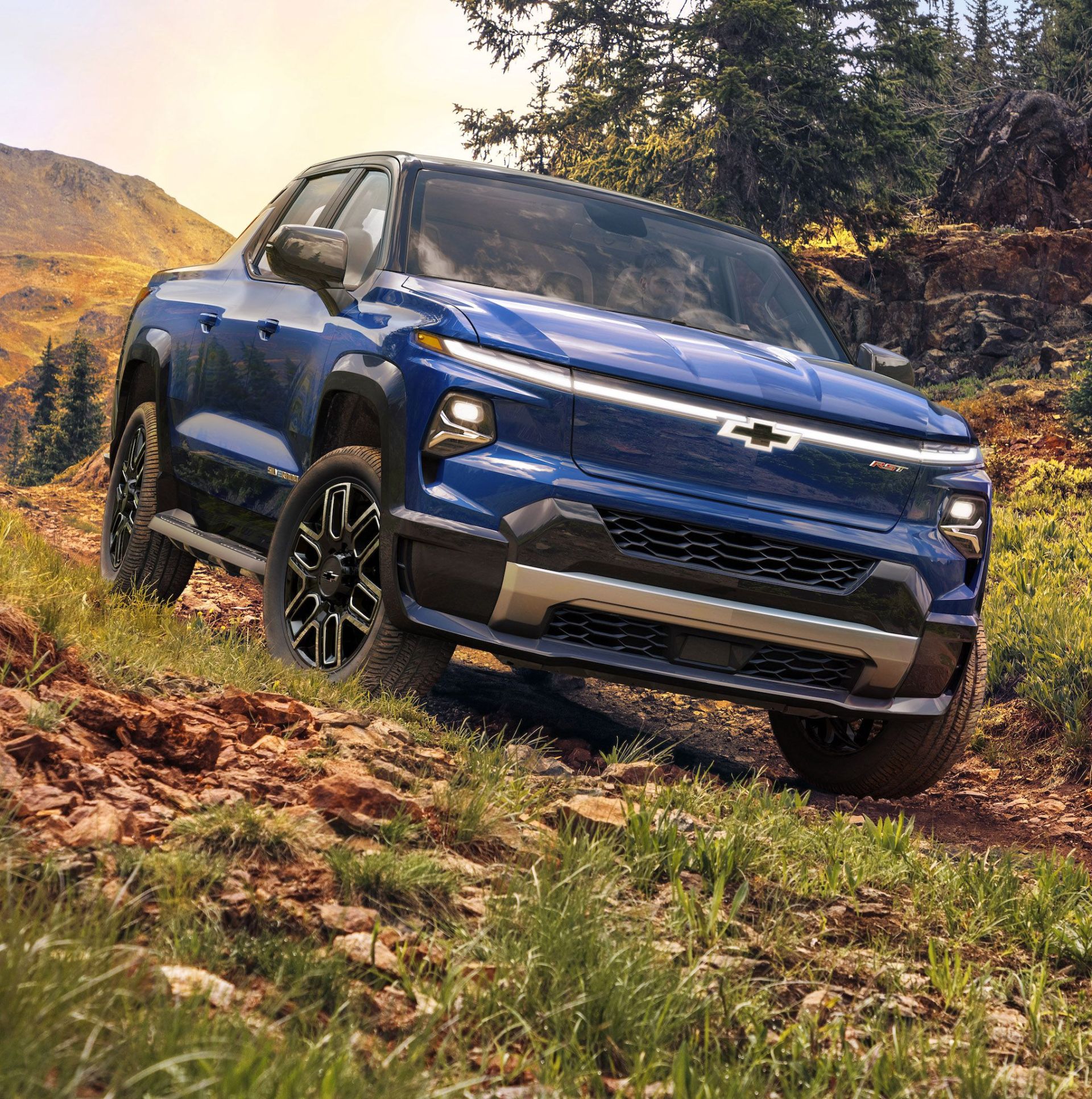chevrolet 2024 silverado ev driving on a wooded path with trees and mountains in the background