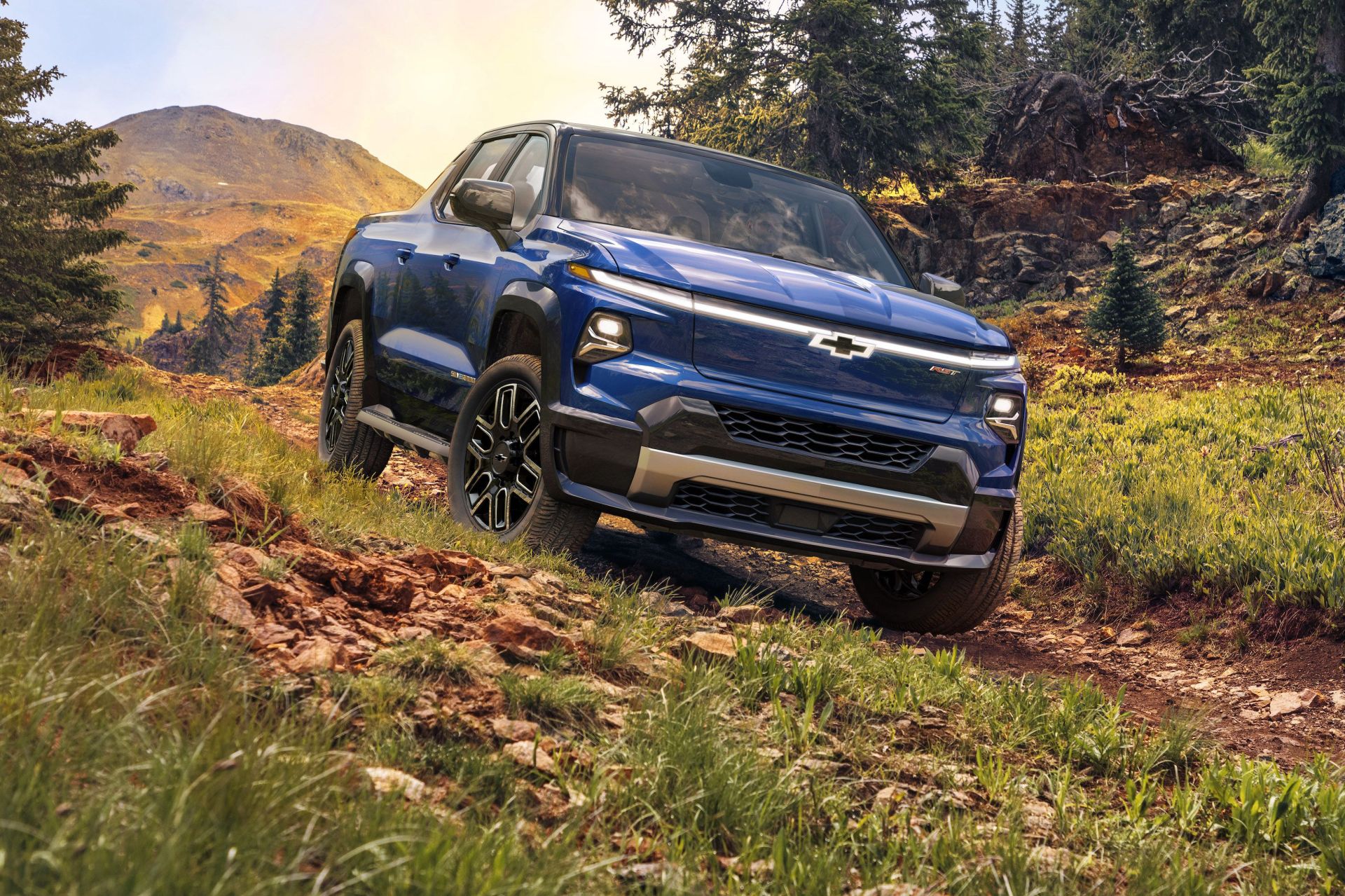 chevrolet 2024 silverado ev driving on a wooded path with trees and mountains in the background
