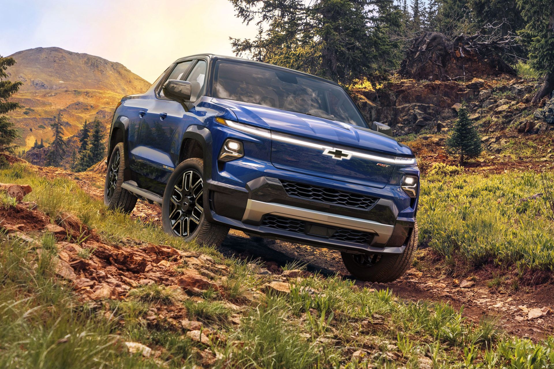 chevrolet 2024 silverado ev driving on a wooded path with trees and mountains in the background