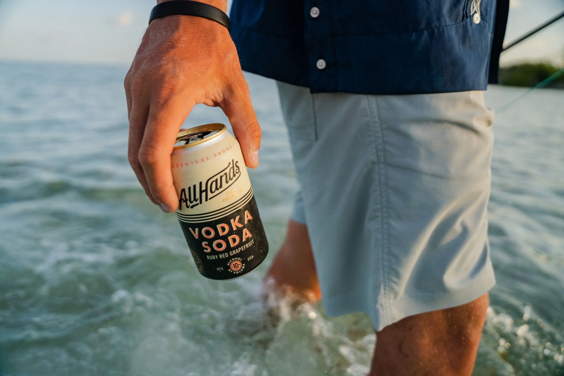 man standing in lake holding all hands craft cocktails vodka soda