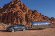 bowlus terra firma camping trailer being towed by a tesla model x and parked in front of a red rock formation