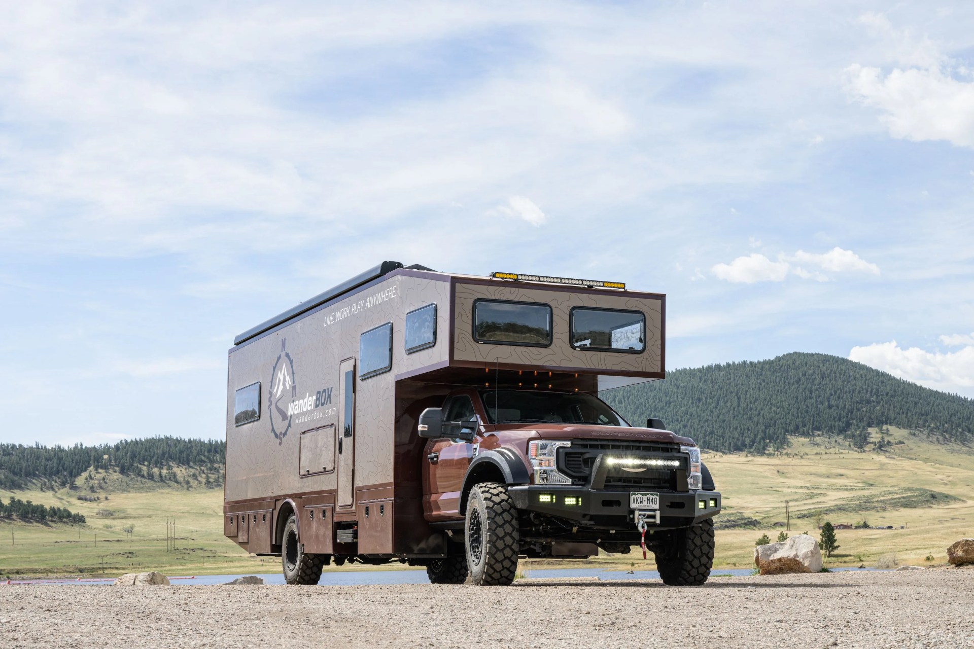 wanderbox outpost camper parked on an off road trail with a pond and tree covered mountain in the background