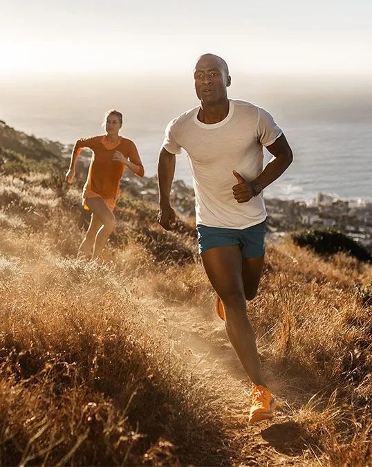 man and woman running through field wearing hoka's tecton x trail running shoe