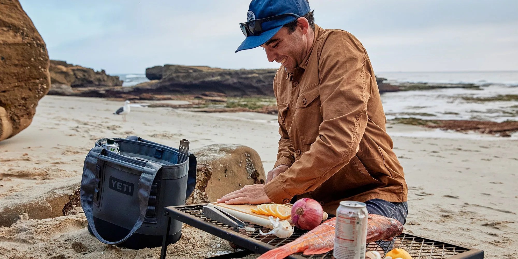 man cutting fish by beachside with yeti camino 20 carryall