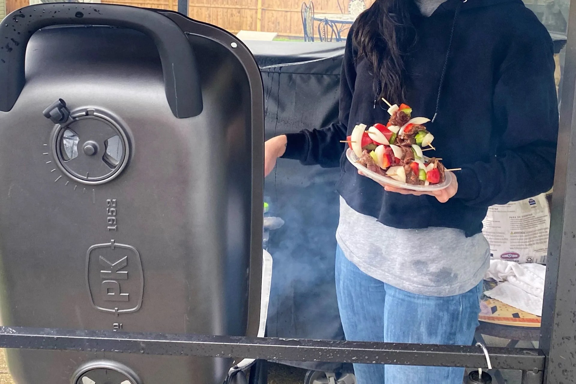 someone standing in front of a griller/smoker while holding a pile of skewers