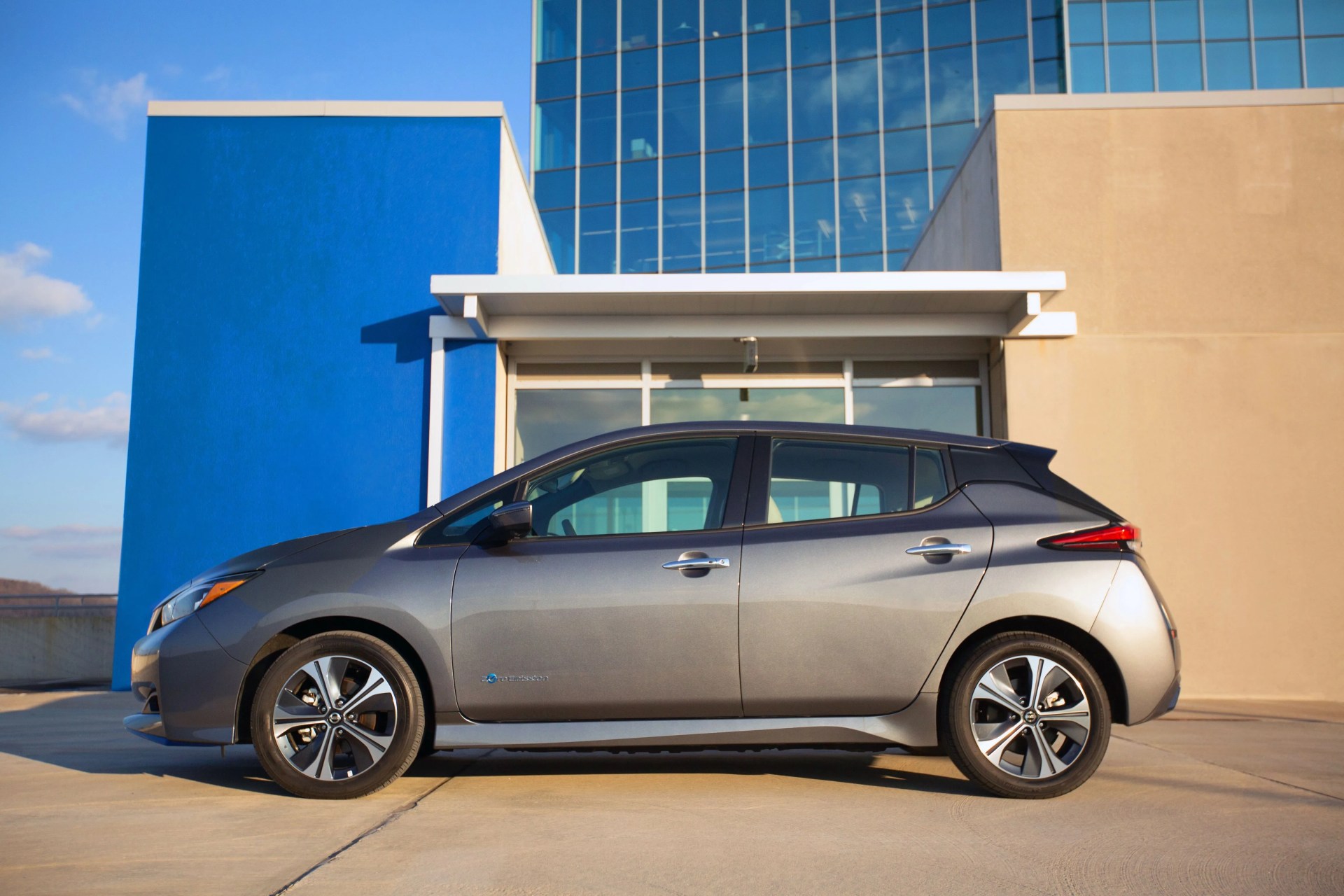 nissan leaf parked on pavement next to a glass building