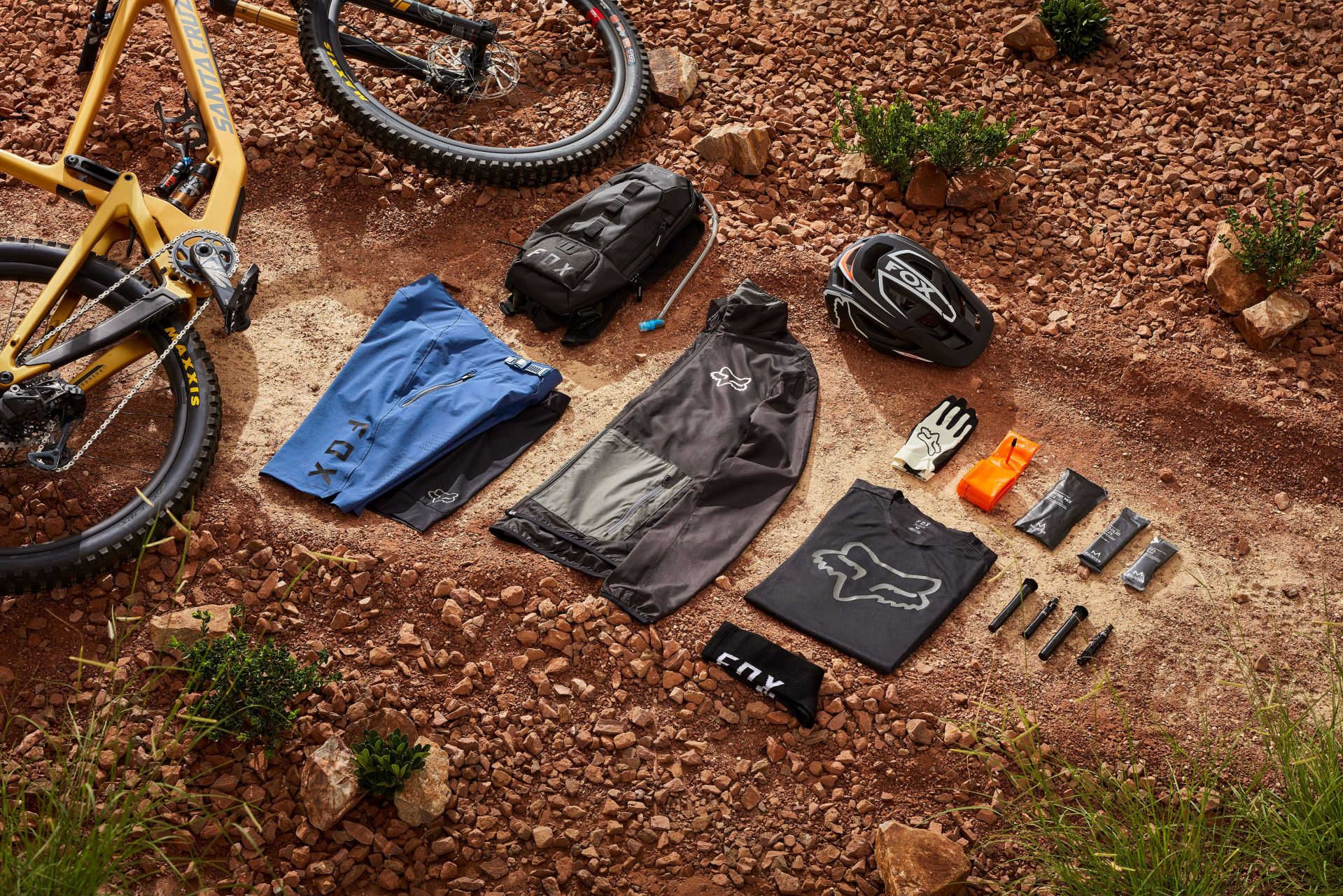 fox racing mountain bike ride kit with bike, helmet, hydration pack, shorts, jacket, gloves, socks, shirt laying in red rock and dirt