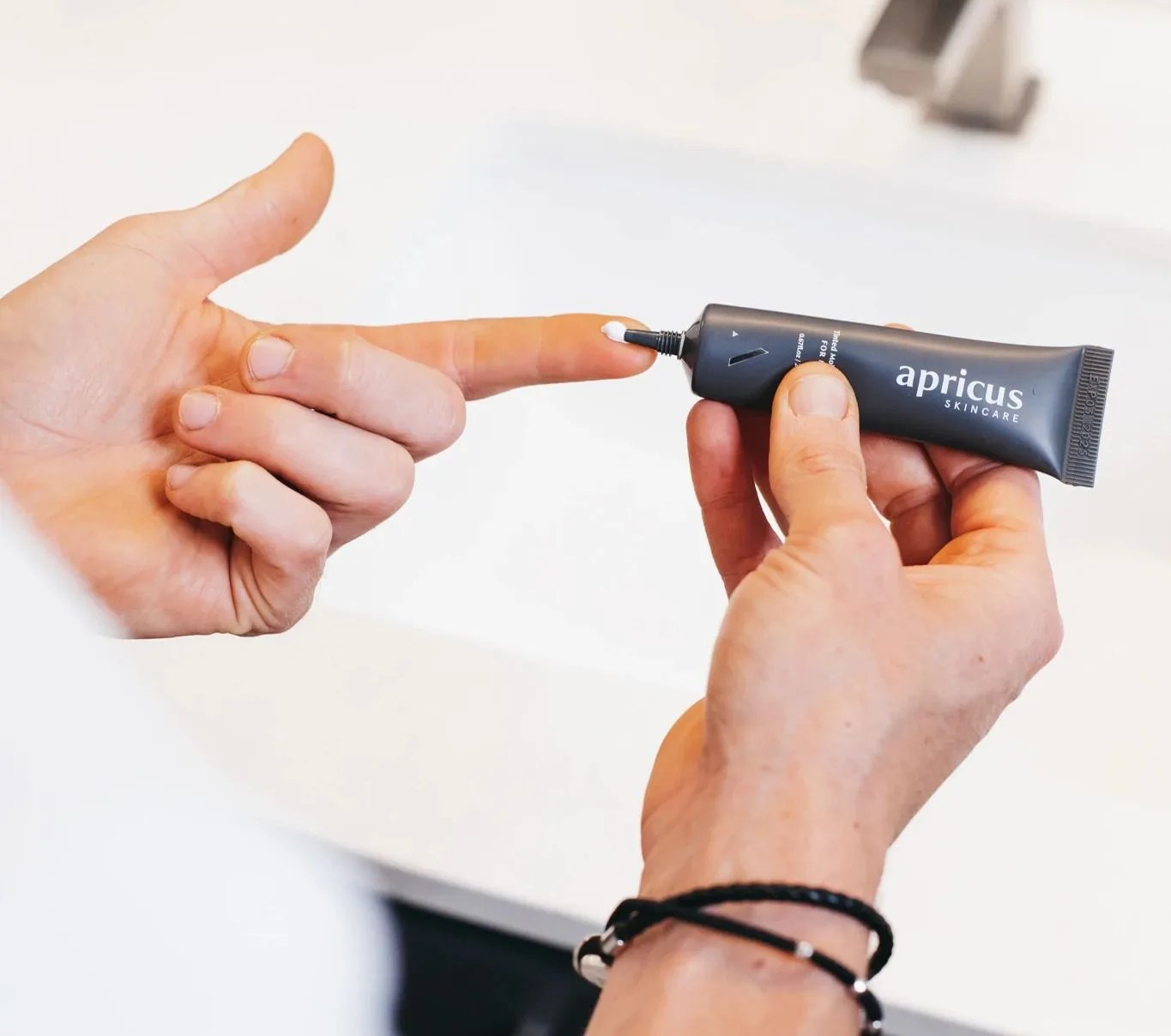 person using a tube of apricus skincare tinted moisturizer