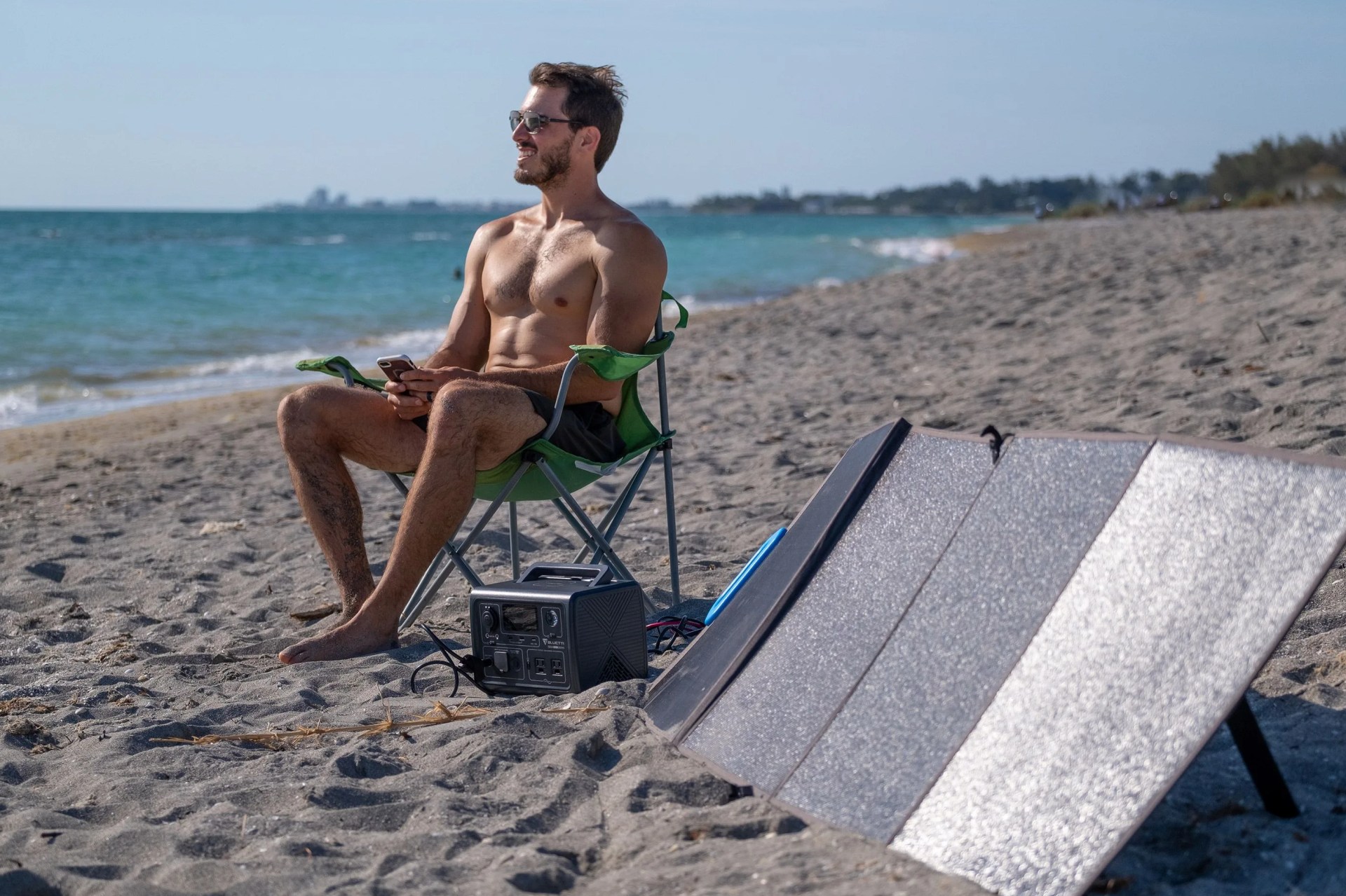 man sitting next to bluetti solar powered generator at the beach