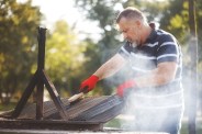 senior man cleaning barbeque during a picnic day