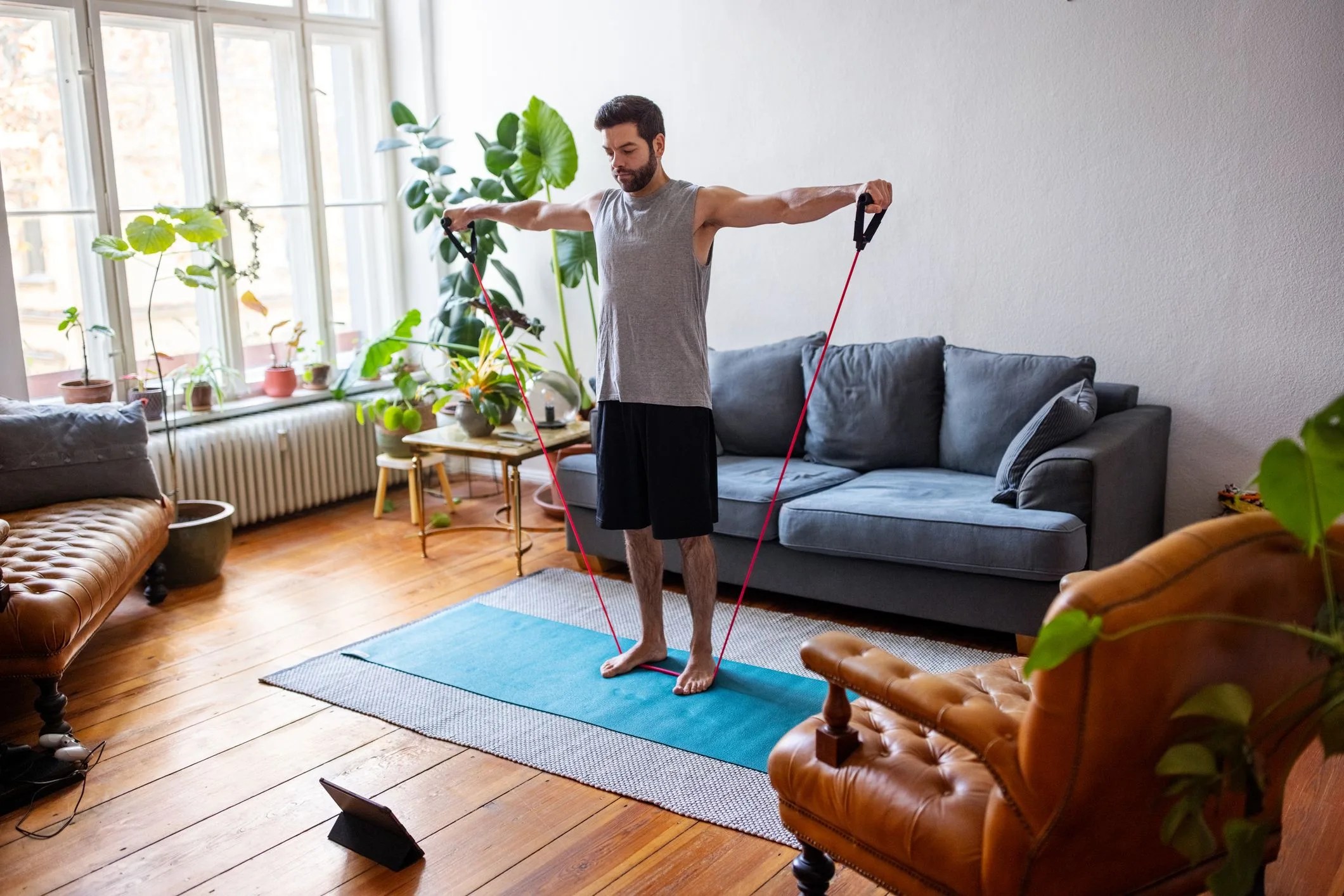man exercising with stretching band at home with a digital tablet mid adult man using an elastic rubber band following a tutorial online and exercise at home during isolation for covid 19 at home