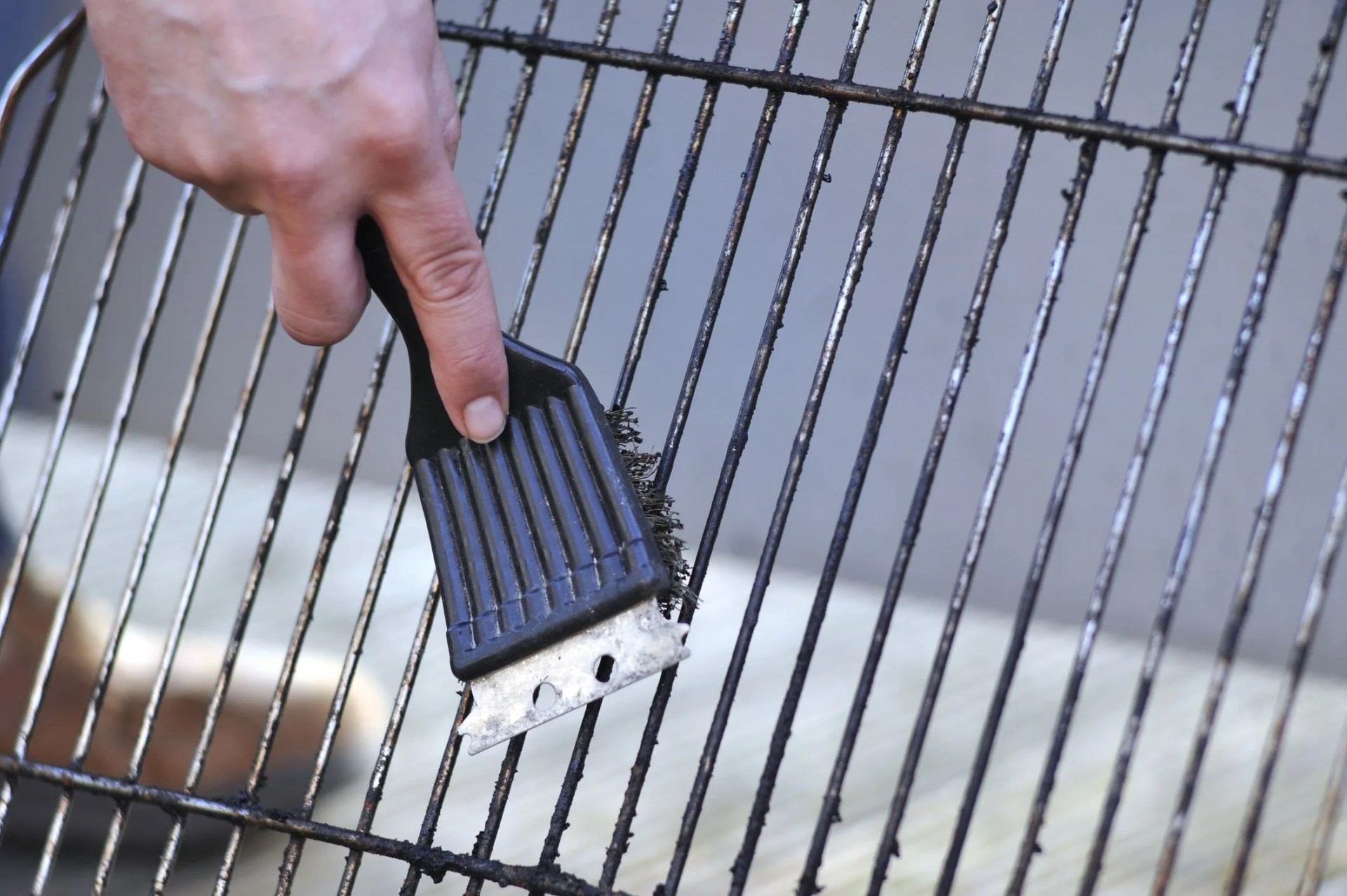 human hand is cleaning the grill rost with scrubber
