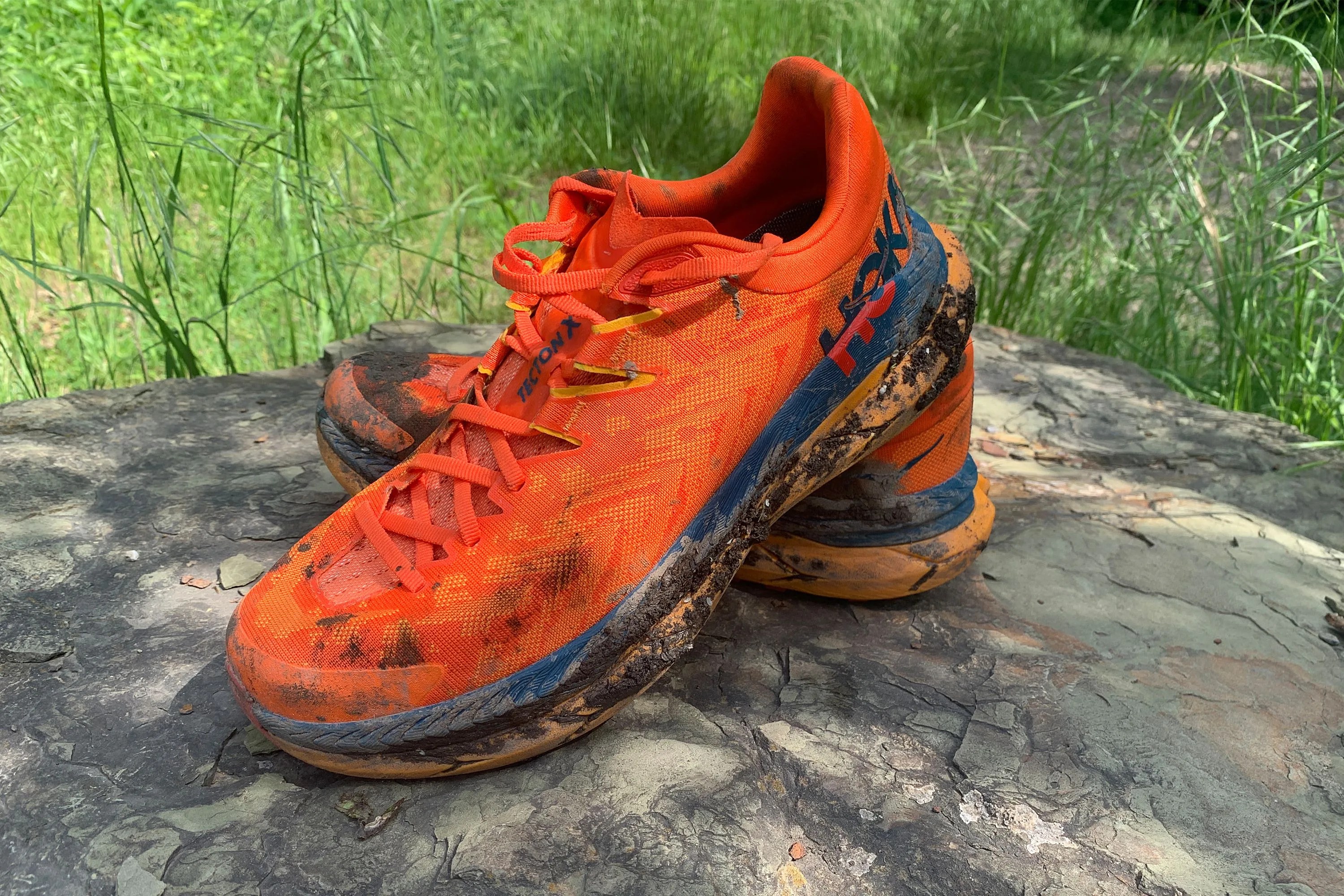orange hoka one tecton x running shoes sitting on a rock
