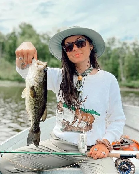 woman sitting in boat holding up fish wearing kayla lockhart signature series sport set