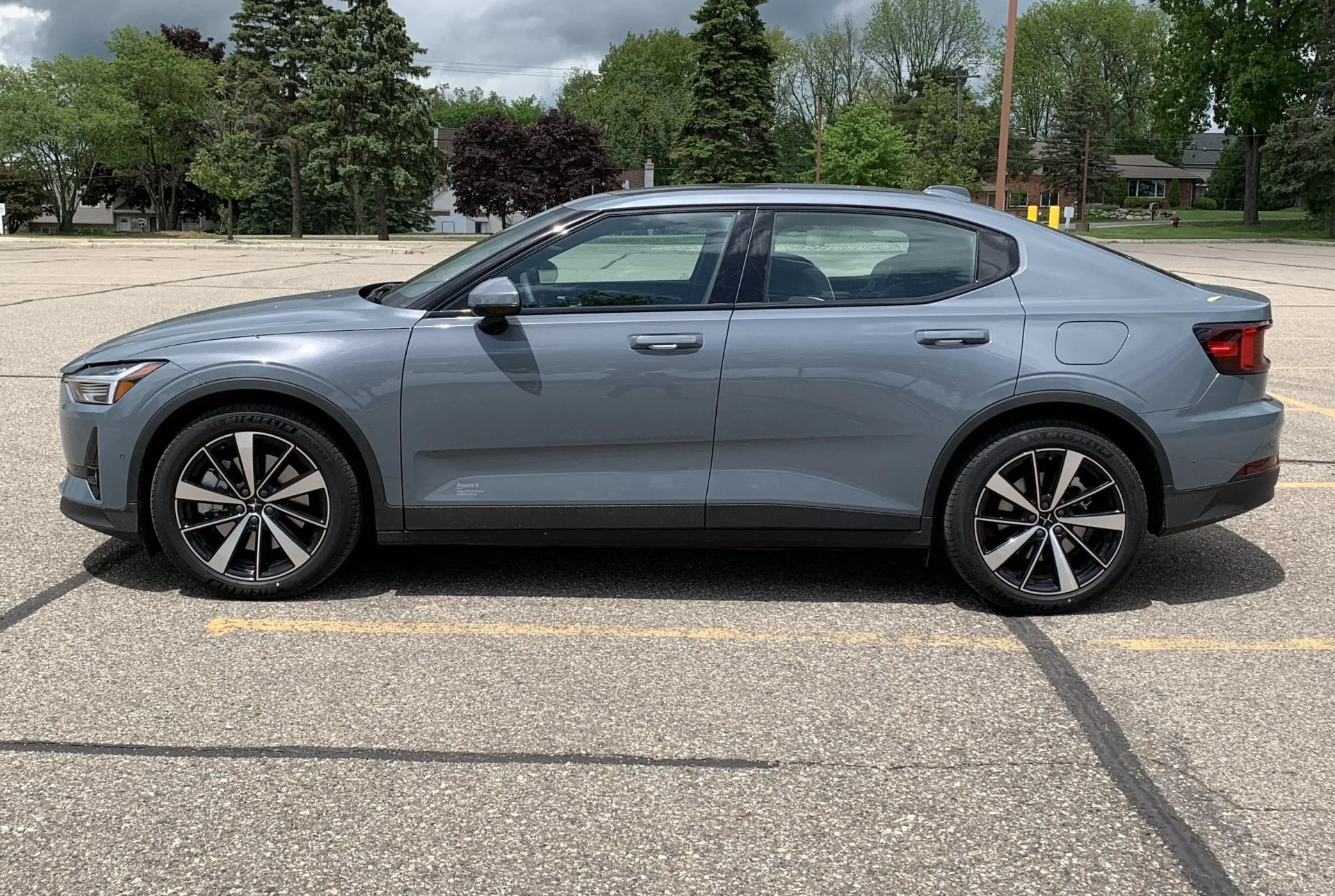 polestar 2 parked in a parking lot in profile with dark clouds and trees in the background