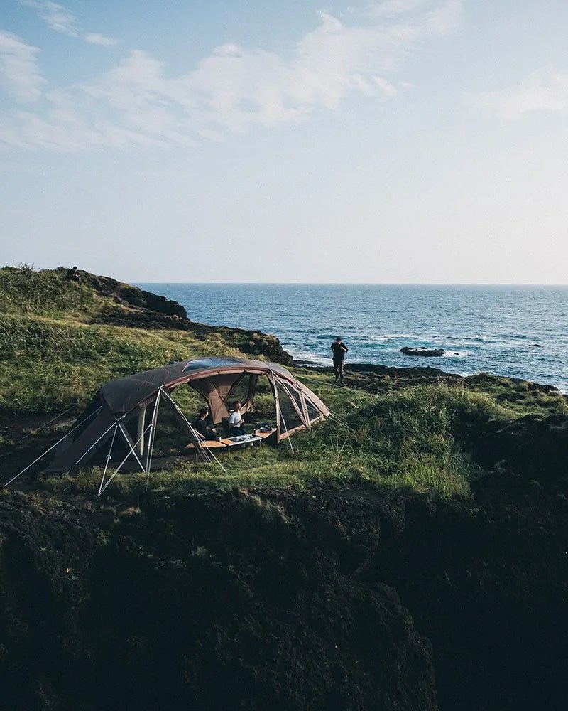 snow peak person using zekka shelter on grass while looking at the ocean in the back
